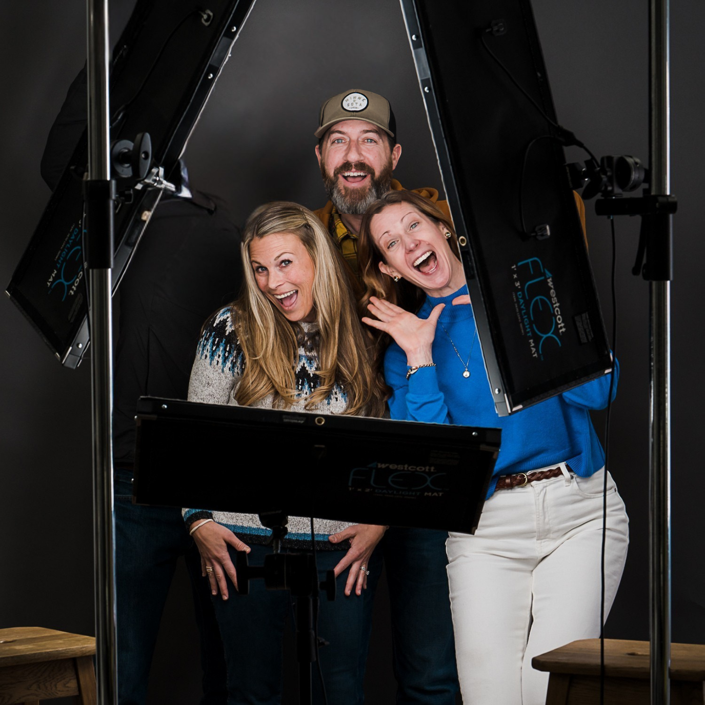 Three people smiling and posing for a photo in a studio setting, surrounded by professional lighting equipment.