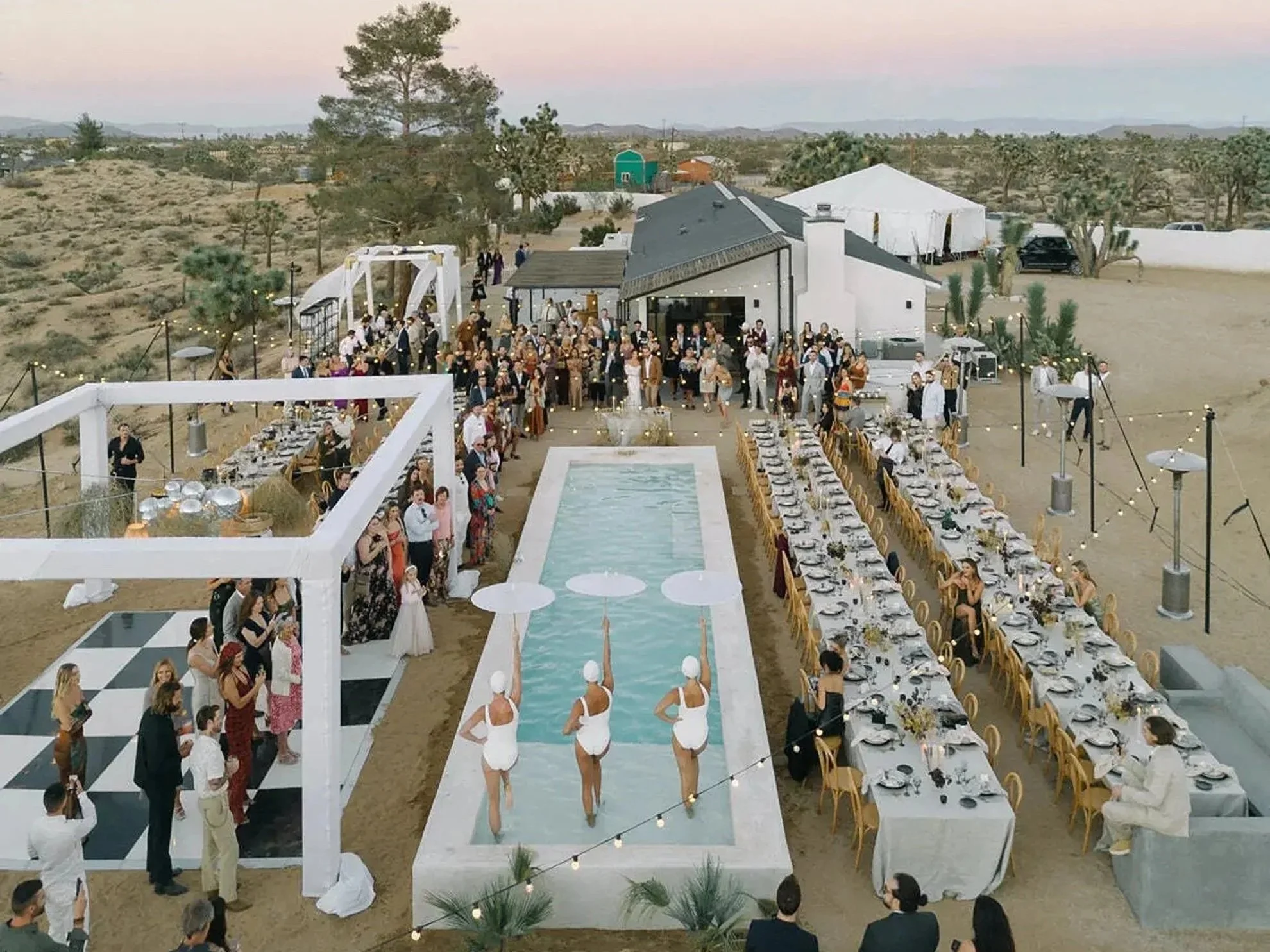 Elevated desert wedding reception set against a scenic desert landscape, featuring a formal banquet-style dining setup with wooden chairs and overhead string lights, thoughtfully designed and produced by a luxury full-service wedding planning team.