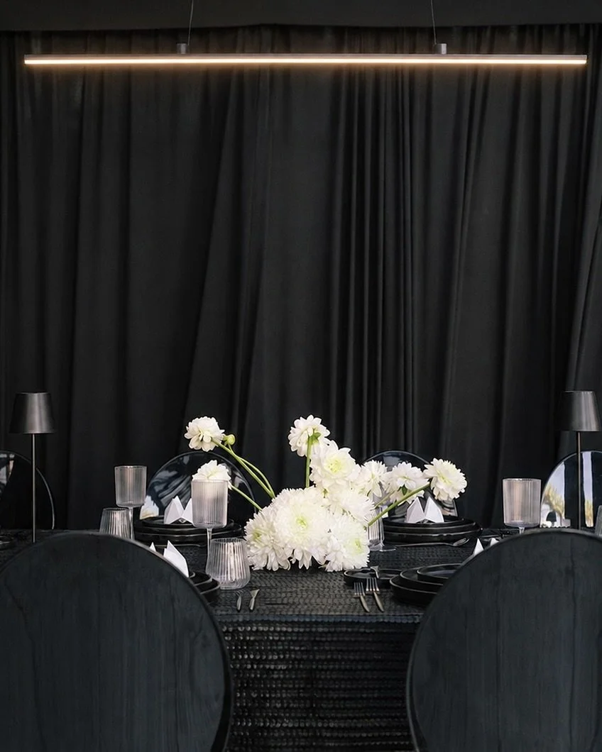 “Modern tented wedding dinner with a monochromatic design, white floral centerpieces, and pendant lighting.”