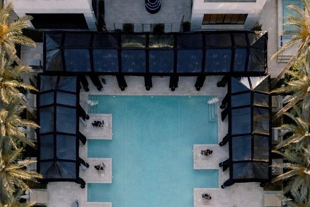 Drone view of a luxury Scottsdale event featuring a custom black clear-top tent surrounding a resort pool with elegant event design, palm trees, and modern lounge spaces