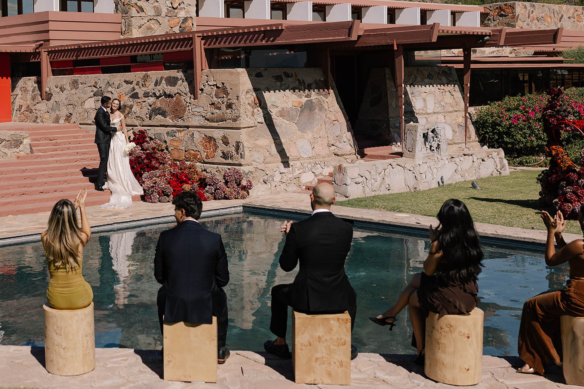 Outdoor wedding ceremony at Taliesin West in Scottsdale, Arizona featuring guests overlooking a fountain, moody modern floral installations, and a couple exchanging vows in a dramatic desert setting.