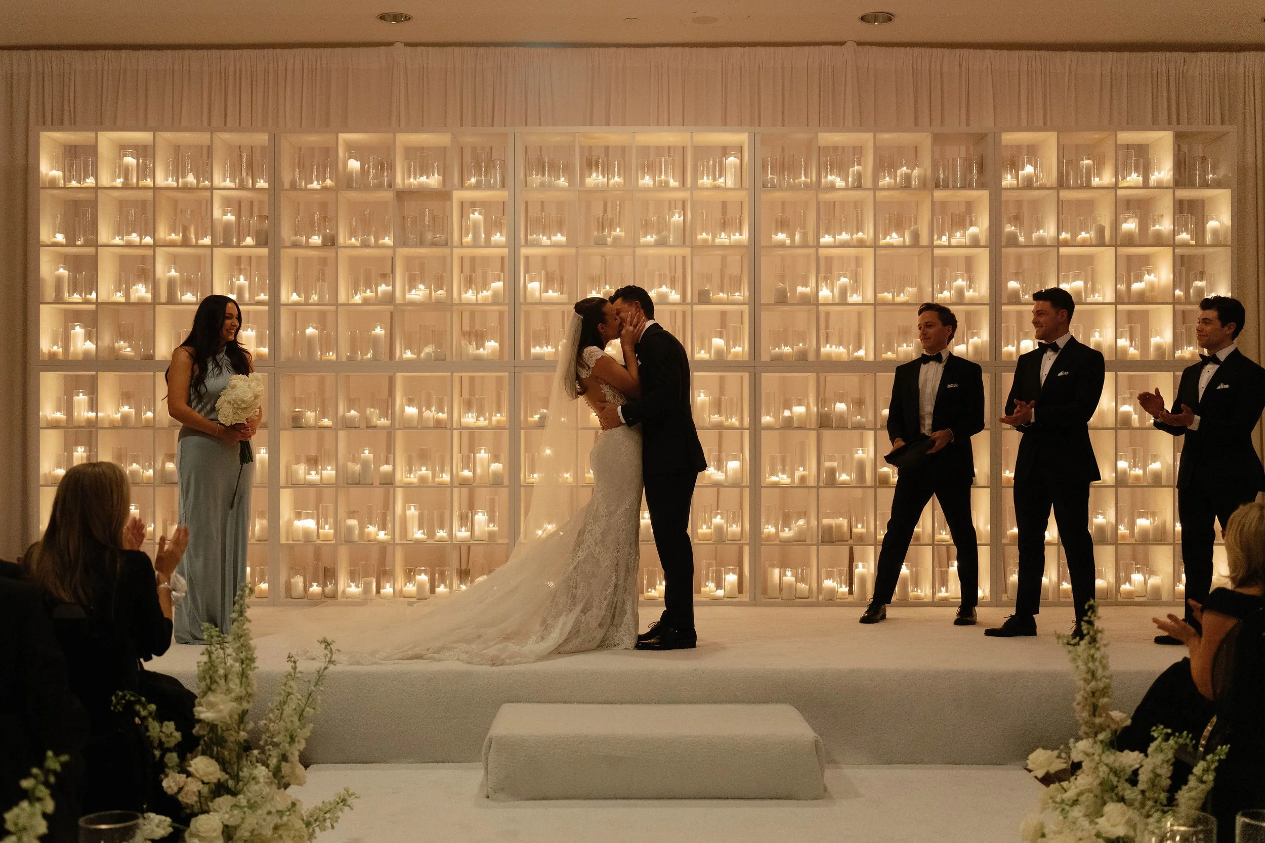 Couple kissing at altar during candlelit ceremony in modern white ballroom at The Camby Hotel.