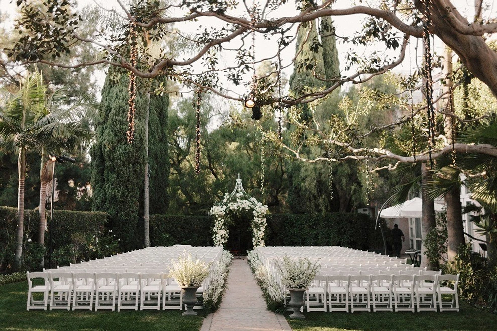 Modern wedding elevated ceremony setup featuring white floral arrangements, white guest seating lining the aisle, and abundant greenery creating a timeless and refined atmosphere, thoughtfully designed by a luxury full-service wedding planning team.