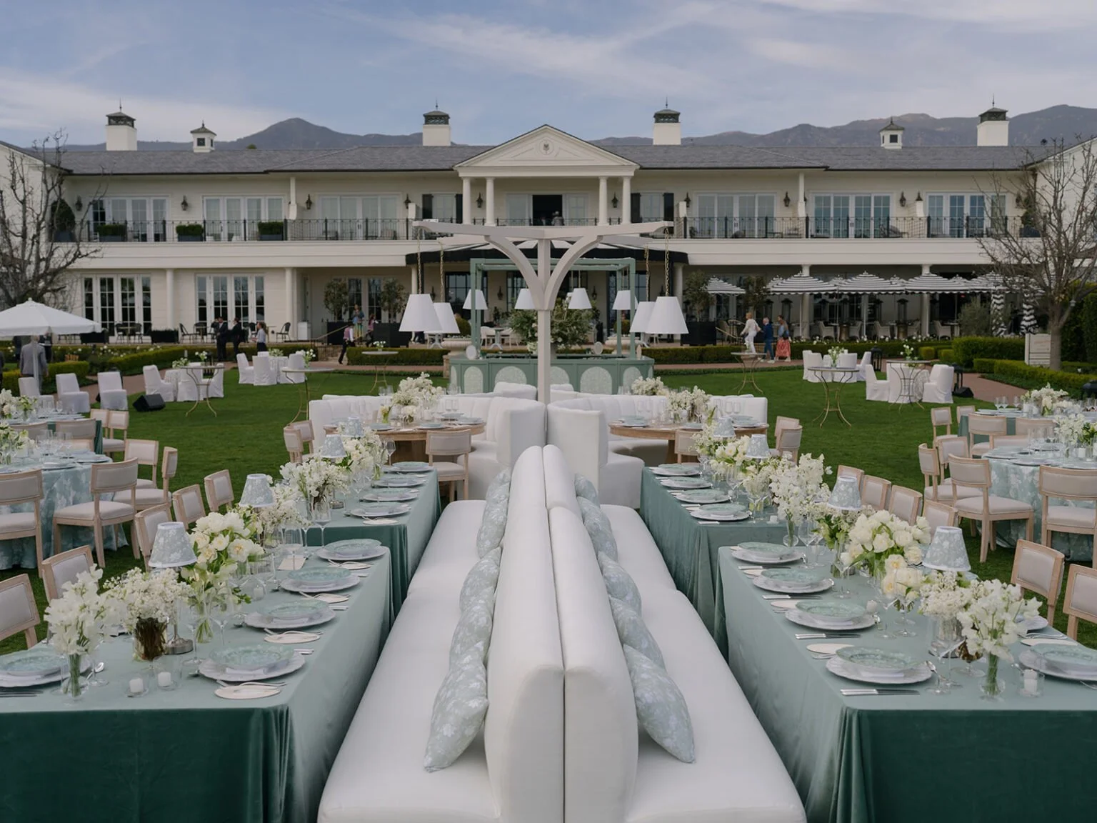 Coastal beach estate wedding reception set in a private backyard, featuring neutral floral arrangements, lounge seating, white table lamps, and blue tablescapes designed by a luxury full-service wedding planner.