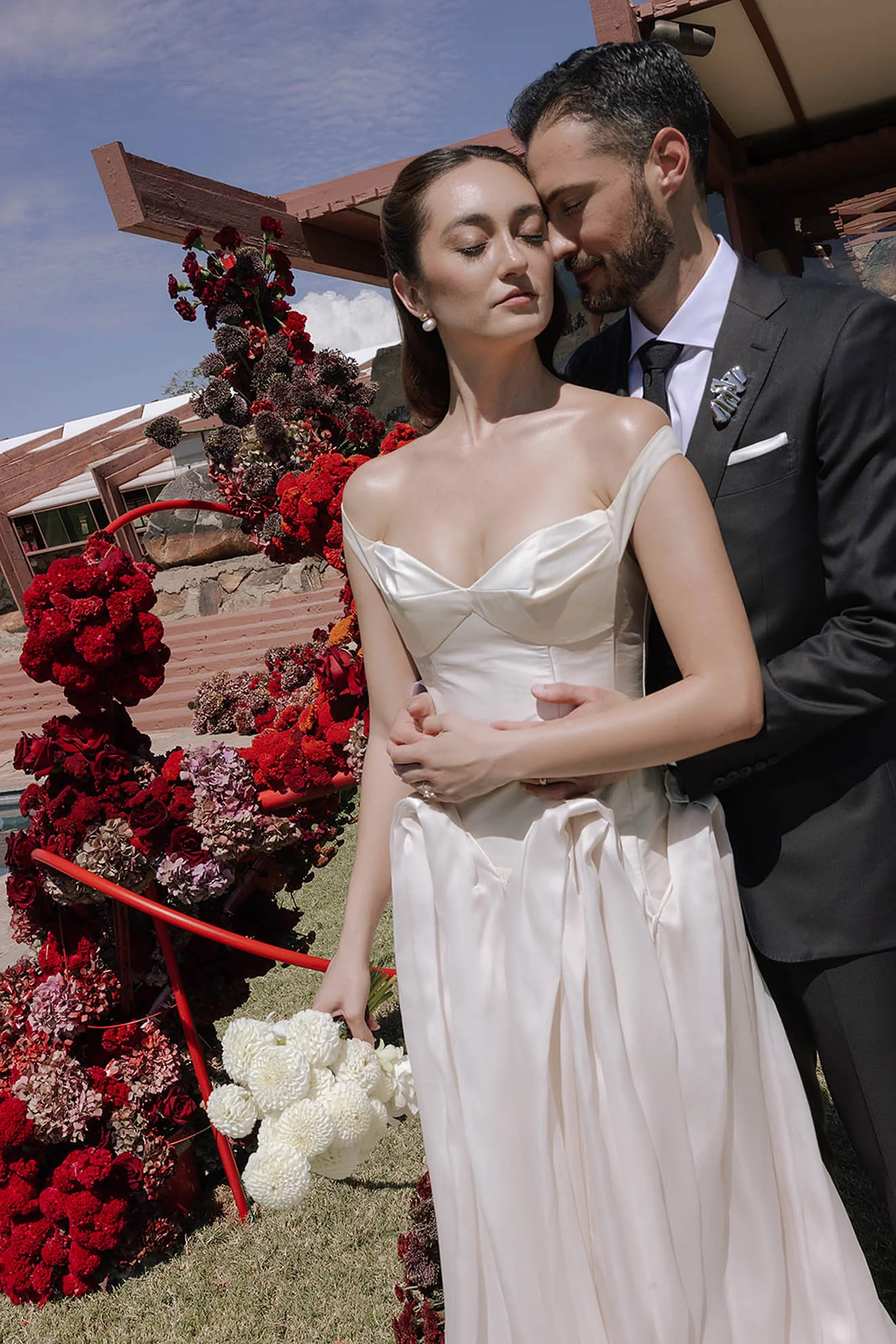 A couple stands in front of an avant-garde floral installation during an outdoor wedding ceremony at Taliesin West in Scottsdale, Arizona, with the bride wearing a J. Andreatta Besette gown surrounded by modern floral design.