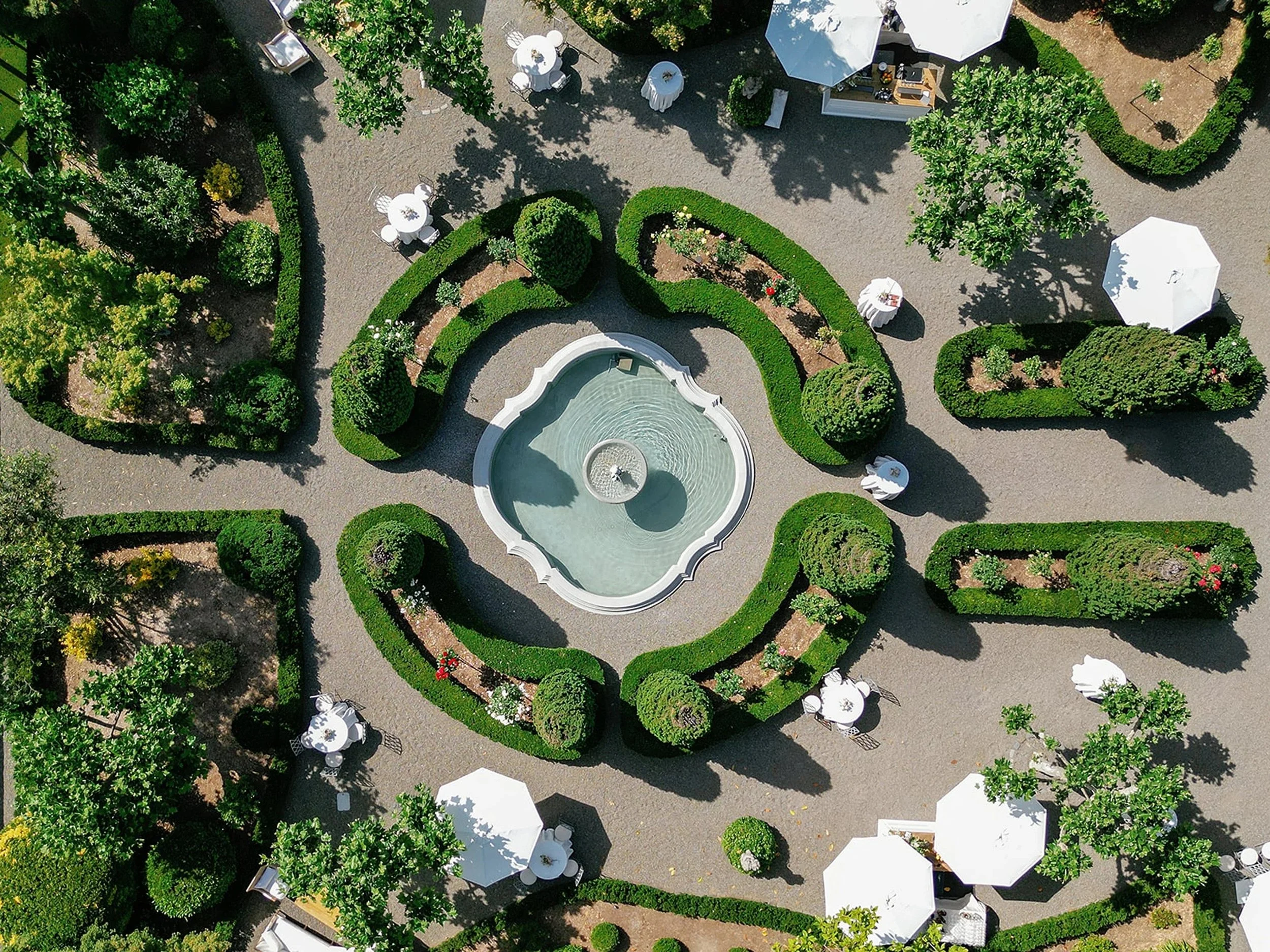 Luxury modern outdoor garden wedding venue featuring white draped high-top cocktail tables, stylish parasols, and meticulously landscaped greenery, curated by a full-service wedding planning and design team.