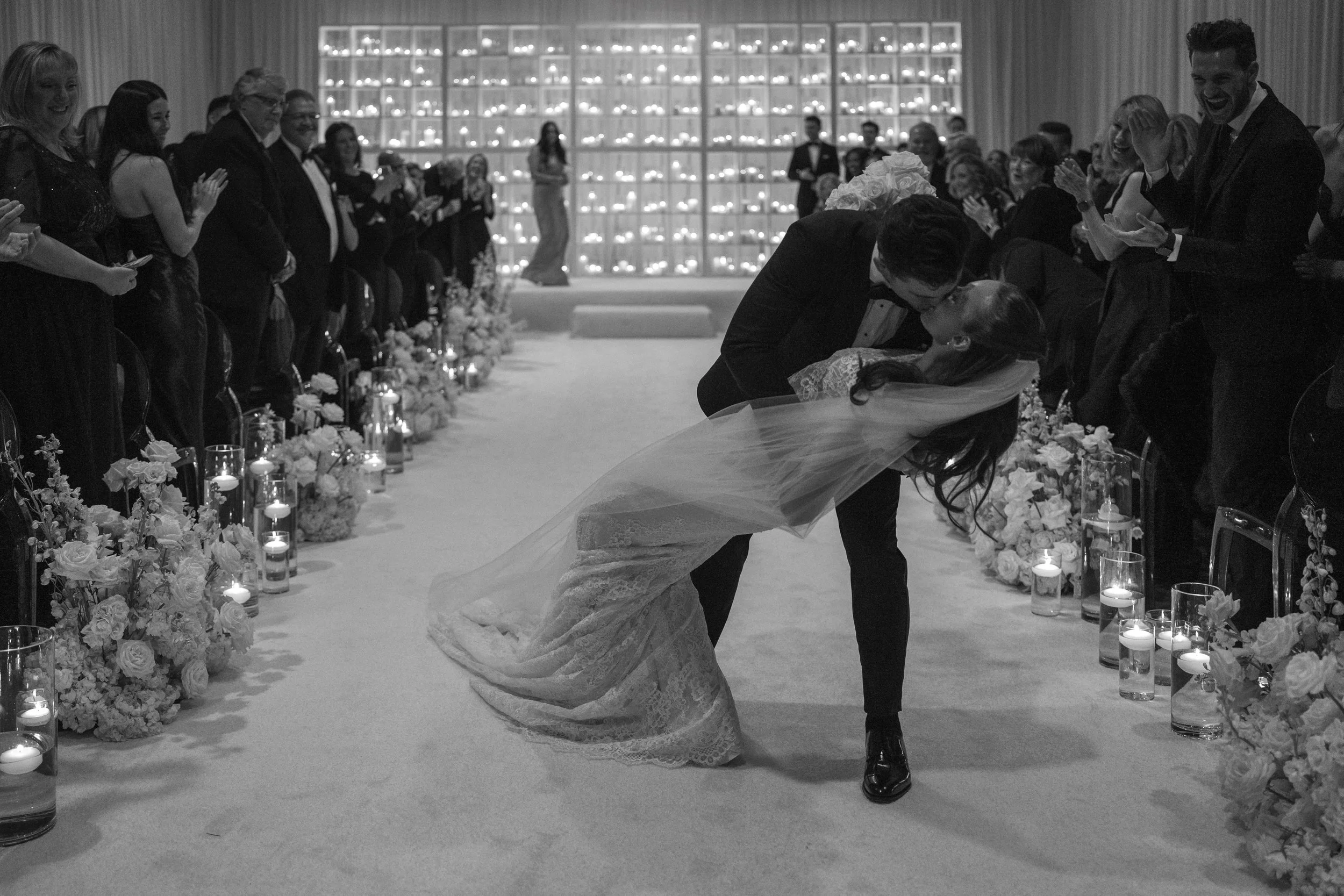 “Couple kissing in the ceremony aisle before a wall of 1,000 real candles at The Camby in Scottsdale, Arizona, with the bride wearing an Ines Di Santo gown.”