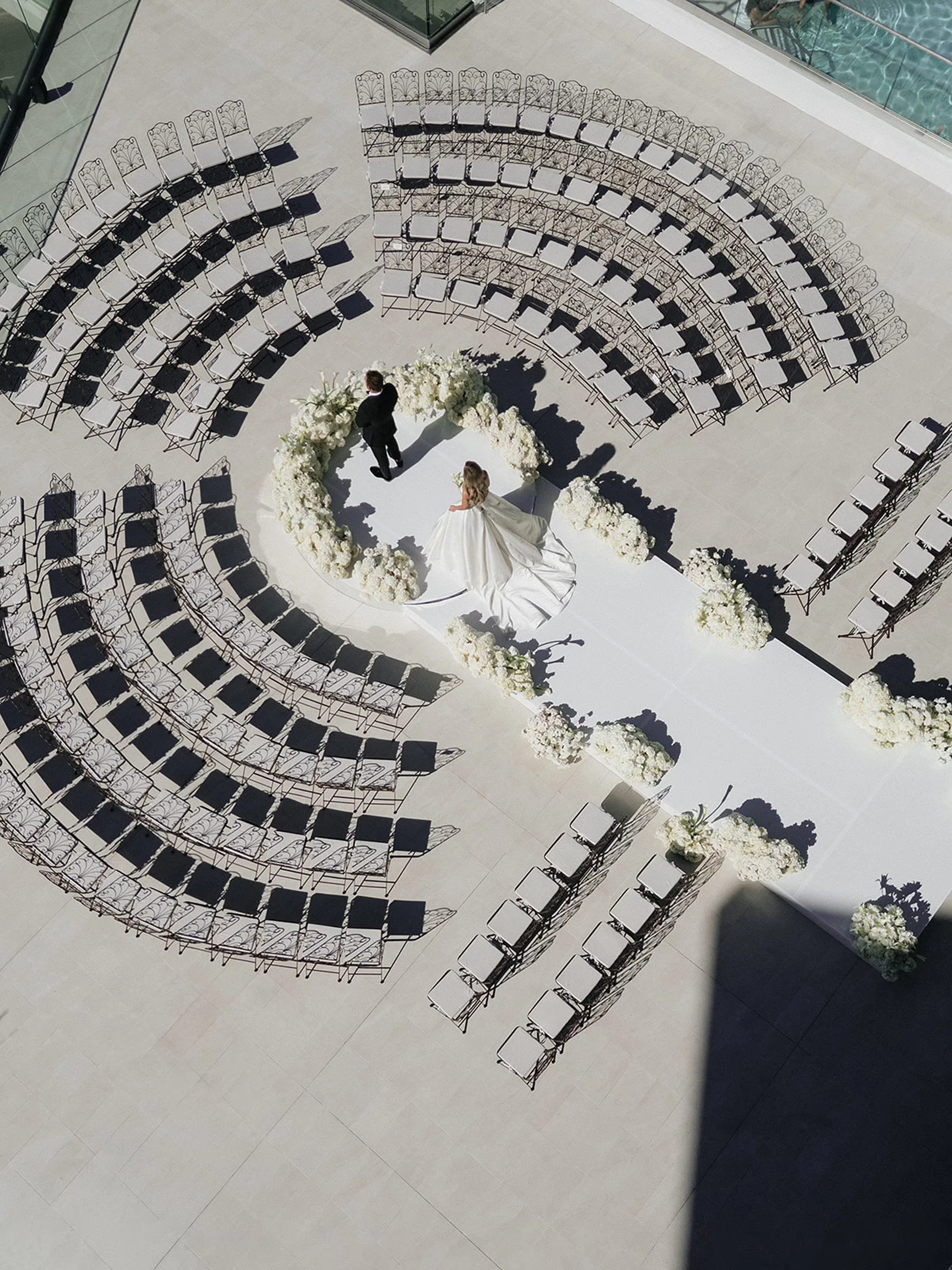 Aerial view of a luxury white wedding ceremony with circular seating as the couple enters for their first look
