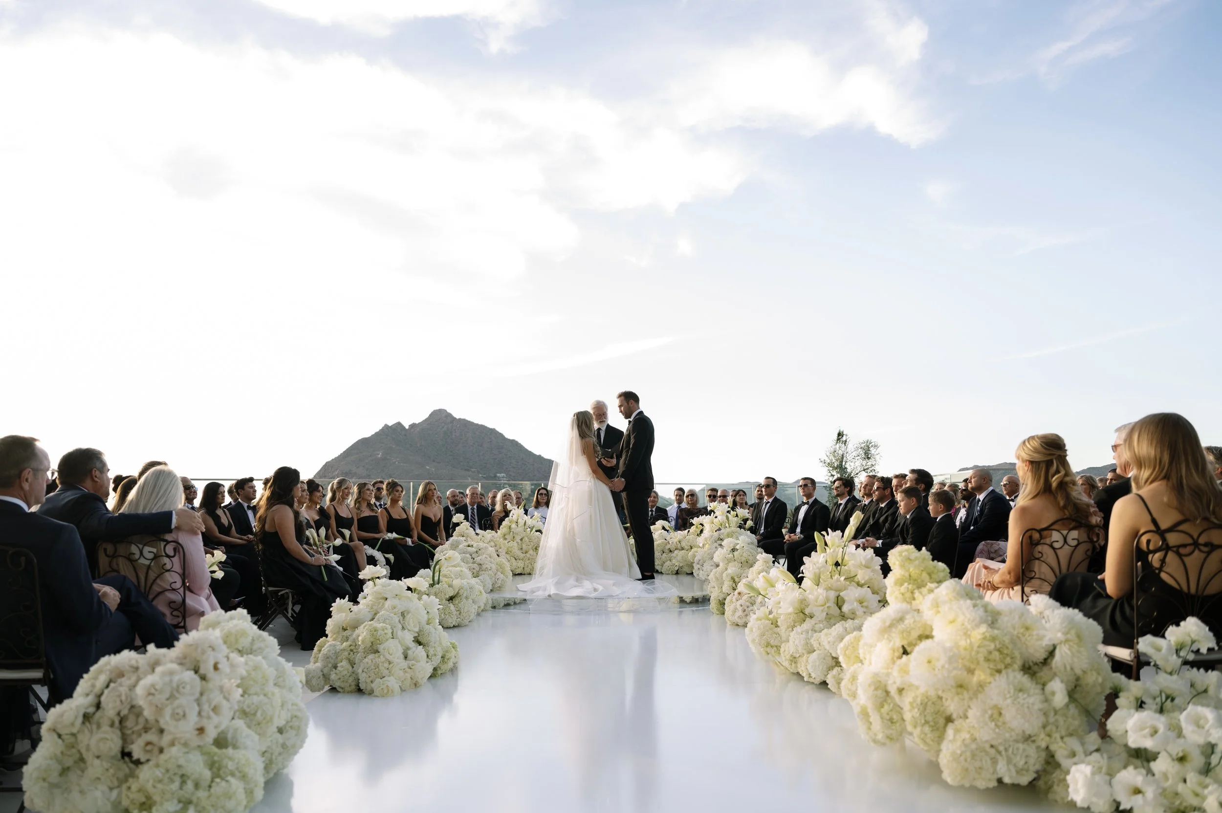 Modern rooftop wedding ceremony in Scottsdale, Arizona featuring a white floral aisle, elevated monochromatic ceremony design, and panoramic desert mountain views.