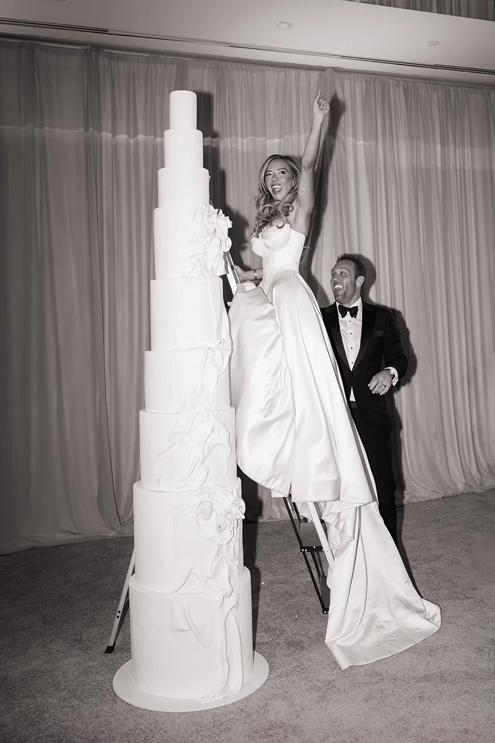 Newlyweds participating in a traditional cake cutting beside an eight-foot wedding cake at Caesars Republic Scottsdale, featuring modern luxury wedding reception design and dramatic presentation.