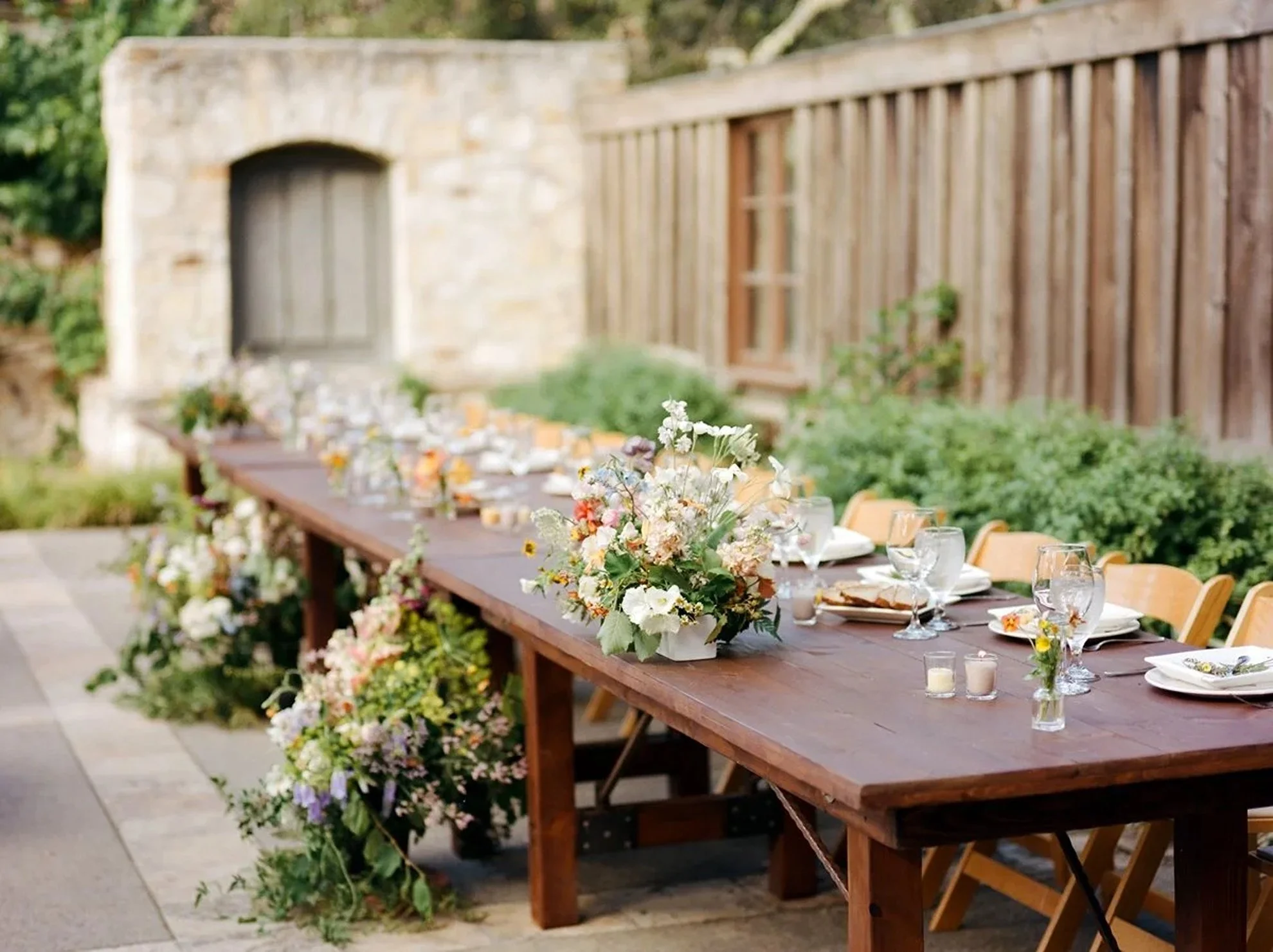 Outdoor wedding reception featuring wooden dining tables and chairs paired with elevated floral centerpieces, thoughtfully designed and produced by a luxury full-service wedding planning team.