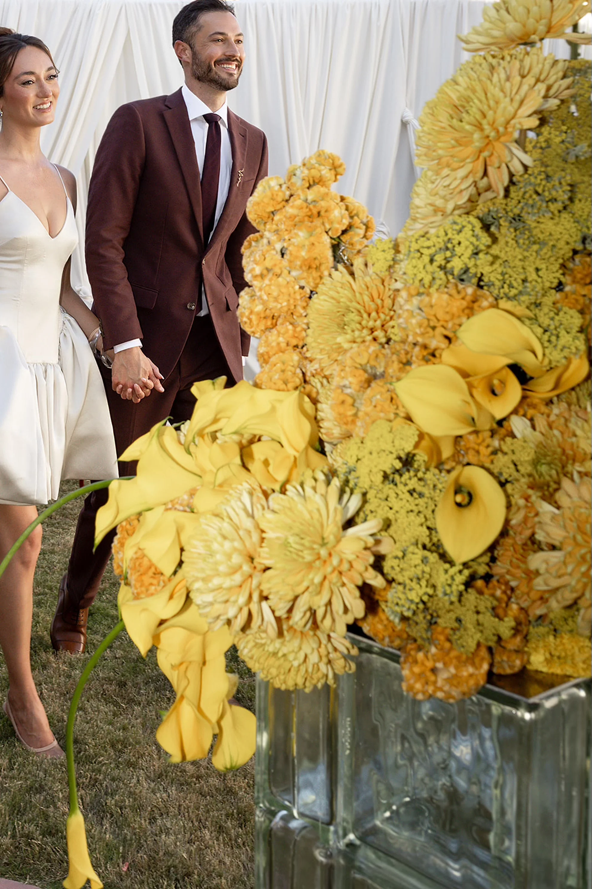 A couple makes their entrance into a luxury welcome party at a historic Frank Lloyd Wright property in Scottsdale, Arizona, featuring modern yellow floral arrangements displayed on a glass mid-century pedestal.