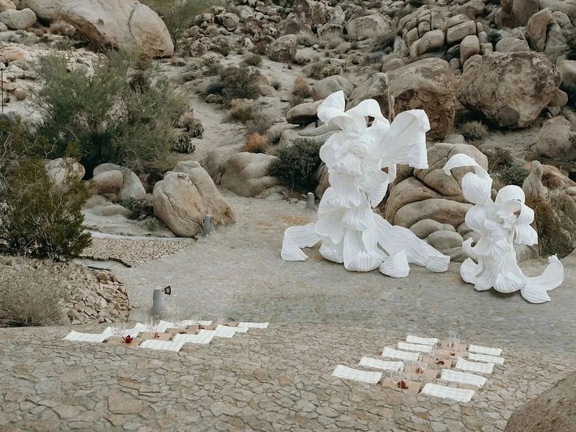 Intimate wedding ceremony set against a dramatic rocky landscape, featuring white sculptural statement installations and tiered stair seating, thoughtfully designed and produced by a luxury full-service wedding planning team.