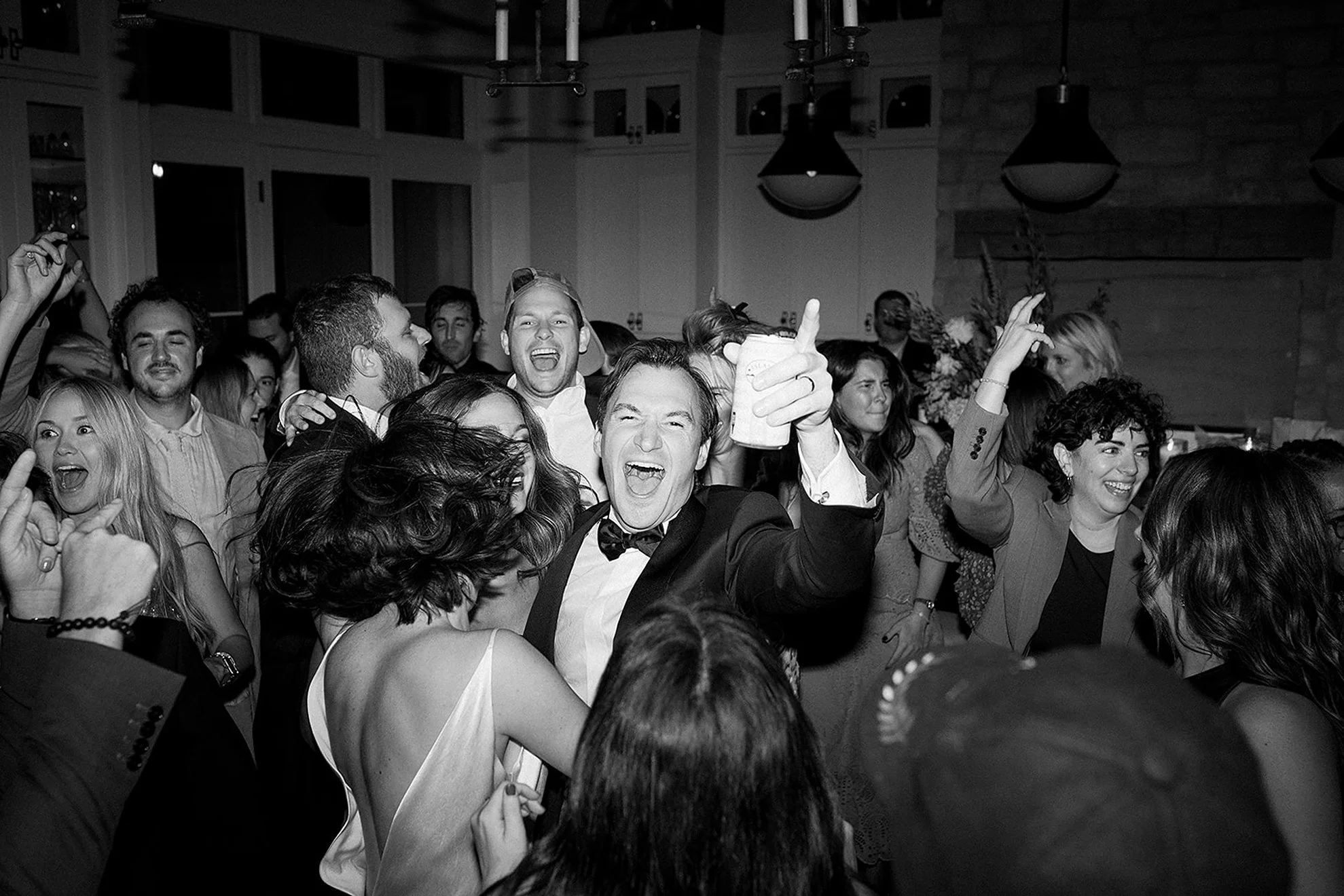 High-energy luxury wedding afterparty with guests and newlyweds jumping on the dance floor during a loud DJ celebration with immersive lighting and vibrant party atmosphere.