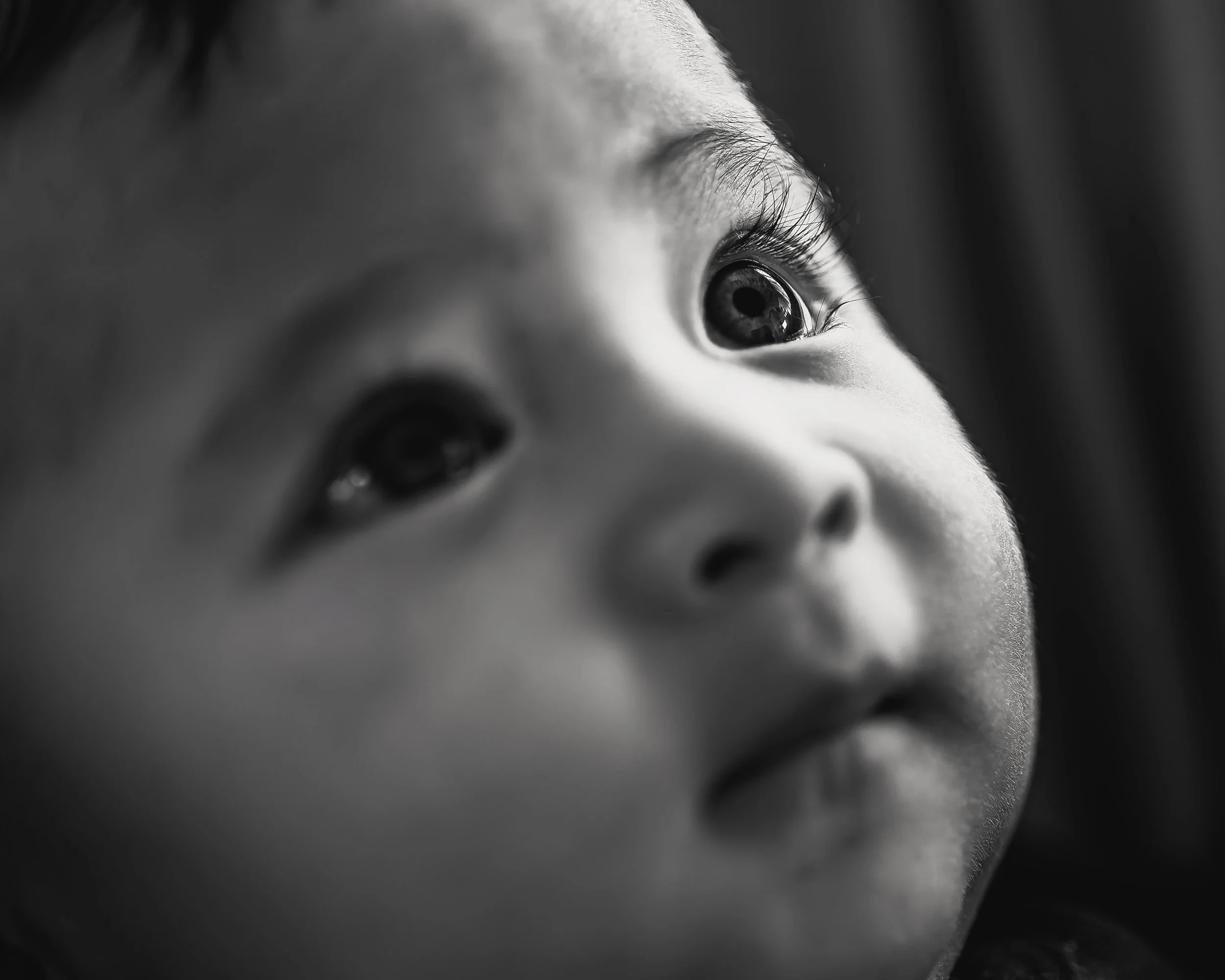 Close-up black and white photo of a child's face, showing large eyes gazing upward.