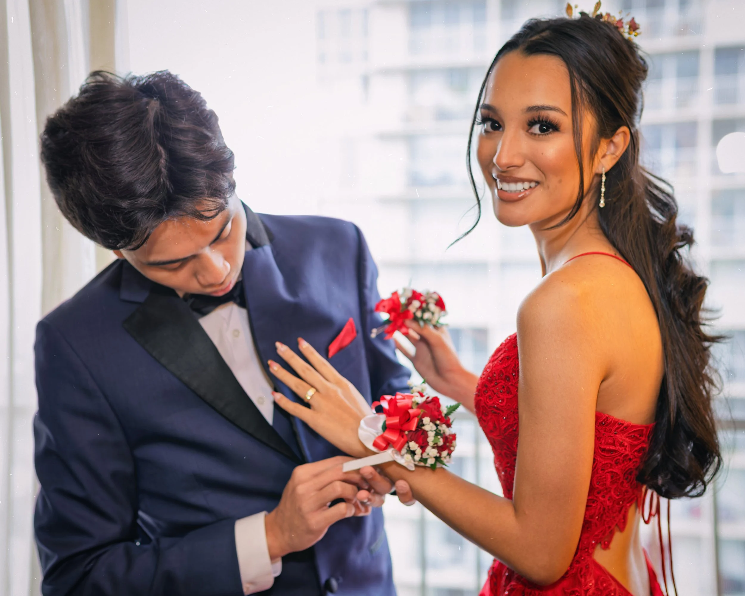 A couple exchanging rings during a wedding ceremony, with the bride smiling and wearing a red dress, and the groom adjusting his suit.