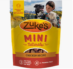 Zuke's Mini Naturals Chicken Recipe dog treats package with a woman and a dog outdoors.