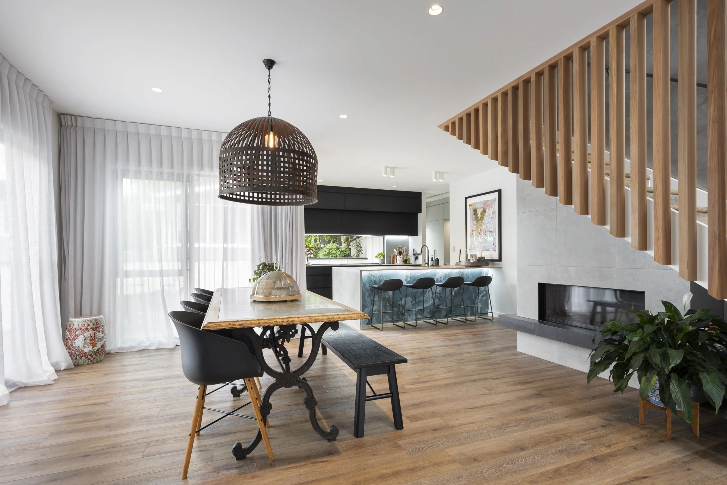 Modern open-concept living space with wood flooring, a dining area, a kitchen with a breakfast bar, and a staircase with wooden railing.