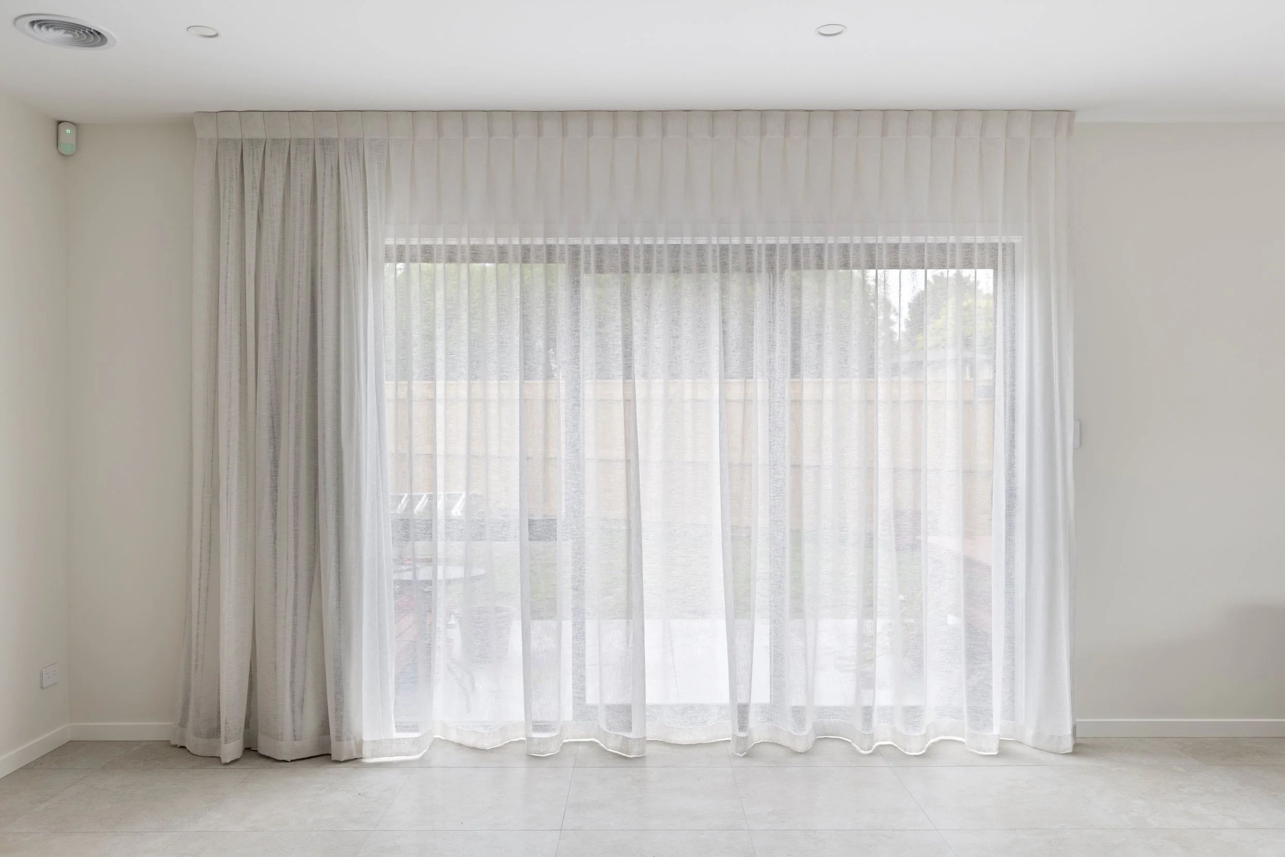 A blank room with sheer curtains showcasing light filtering