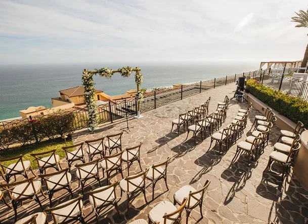 Outdoor wedding ceremony setup with chairs and an arch overlooking the ocean on a sunny day.