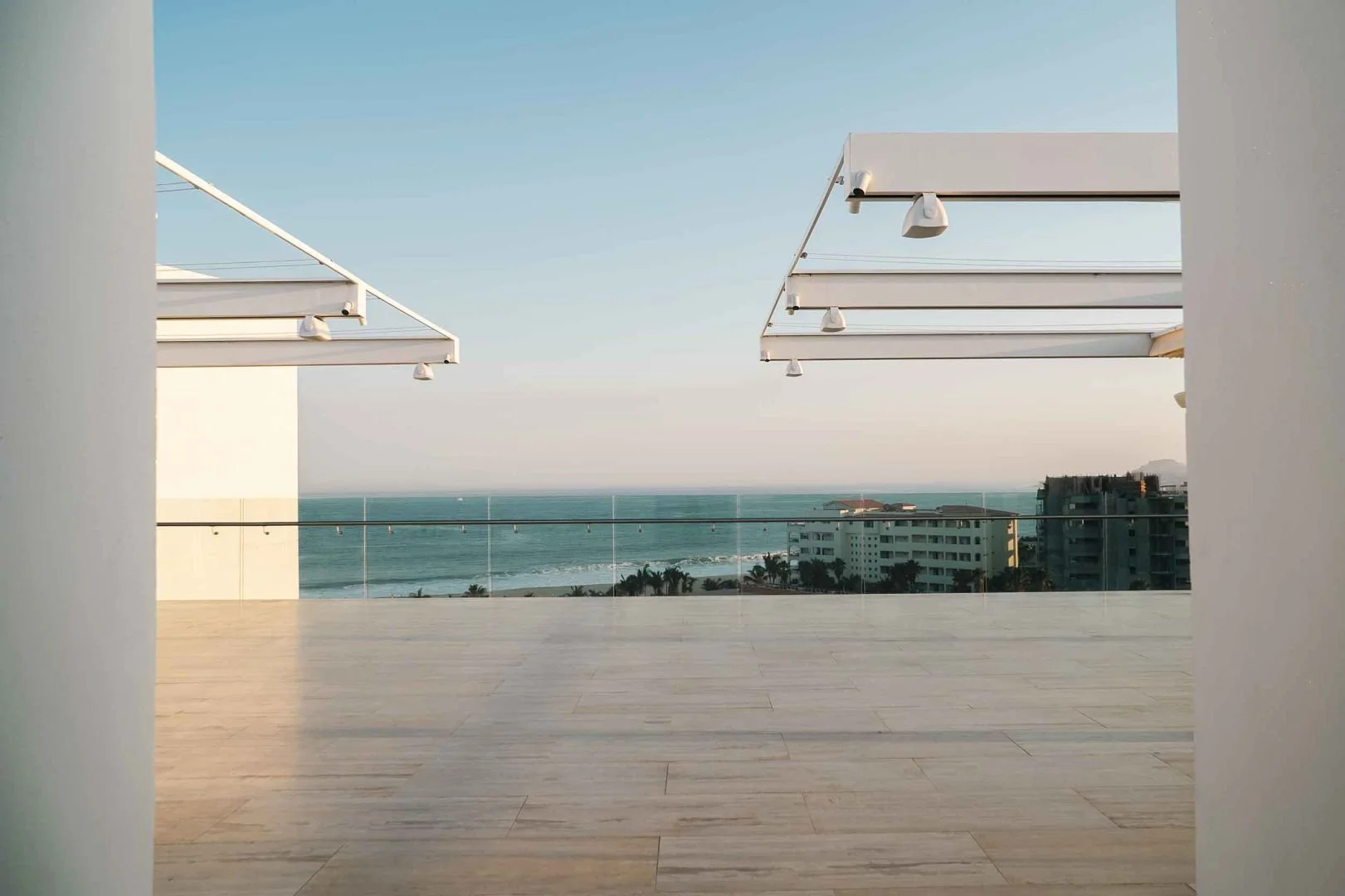 Long outdoor dining table set up with chairs, glasses, and candles along a coastal shoreline at sunset