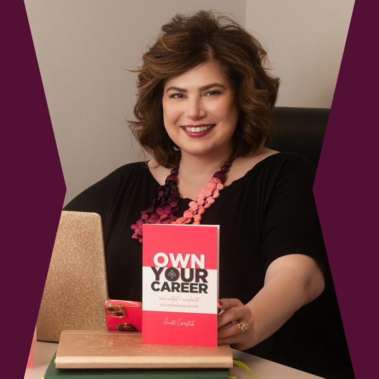 Annette Garsteck is smiling at the camera. She is sitting at a desk with a gold laptop, pink phone, and a notebook. She is holding a pink and white book titled "OWN YOUR CAREER."