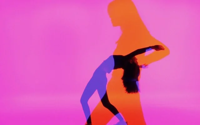 A bright pink bakground with an orange silhouette of a girl standing to the side. Another smaller and purple silhouette of the girl bending back with her arms up is near the front of the image. 
