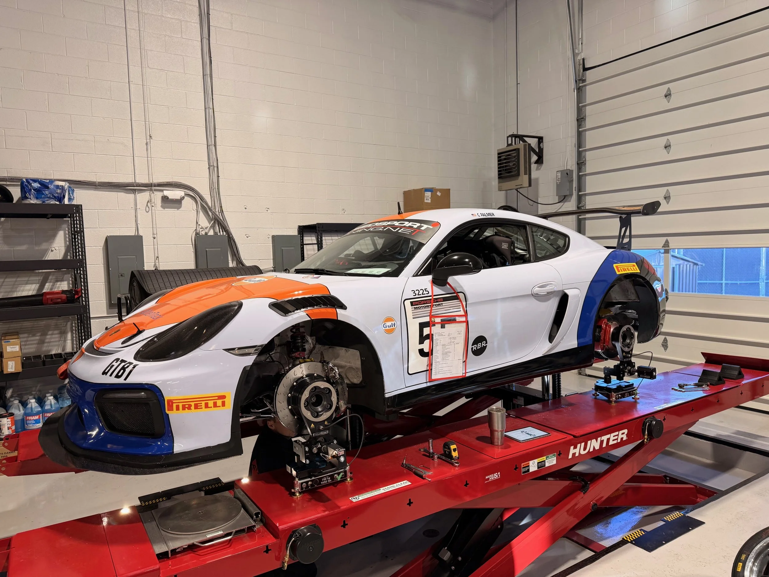 Race car on a red work lift in a garage with tools and shelves in the background.