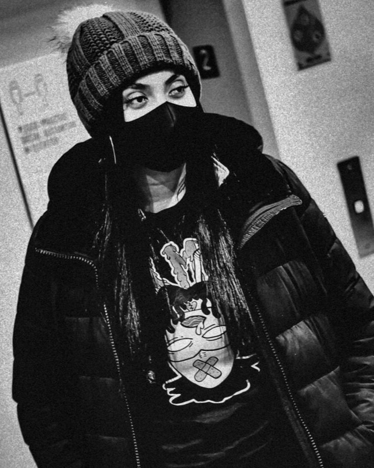 A woman wearing a beanie, face mask, and puffer jacket standing in an elevator.