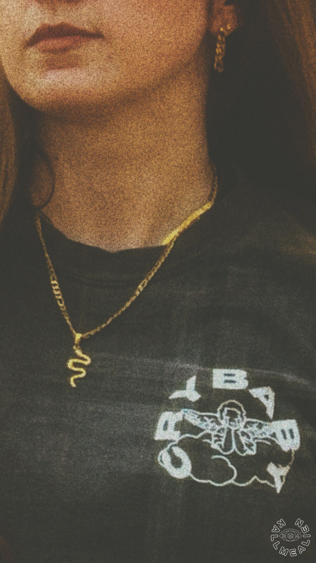 A woman wearing gold jewelry, including earrings and a necklace with a snake pendant, and a black shirt with a white graphic design.
