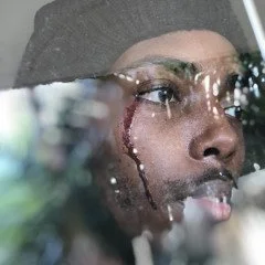 Close-up of a person looking through a rain-covered window, with raindrops on the glass.