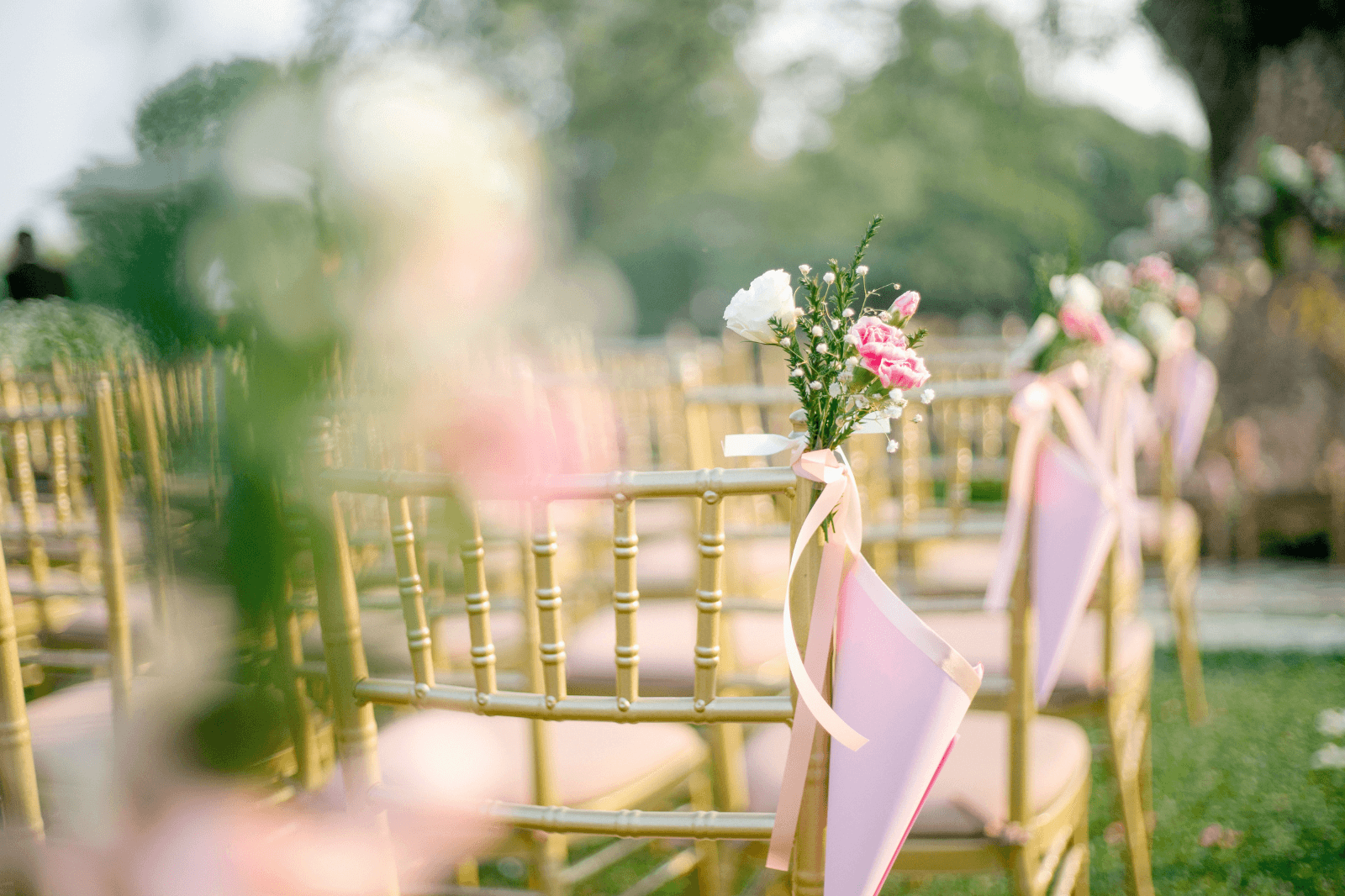 Outdoor wedding ceremony seating decorated with pink ribbons and flowers.png