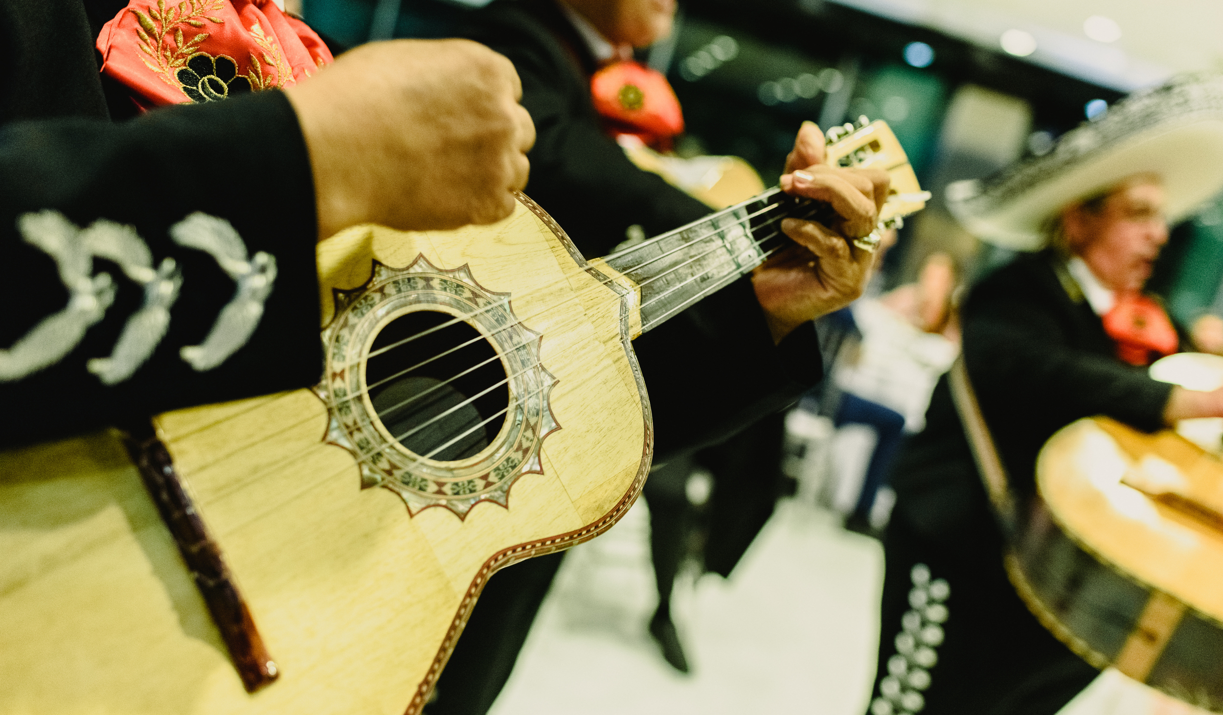 Close-up of mariachi musicians playing guitars in traditional black suits with red bow ties at an event.