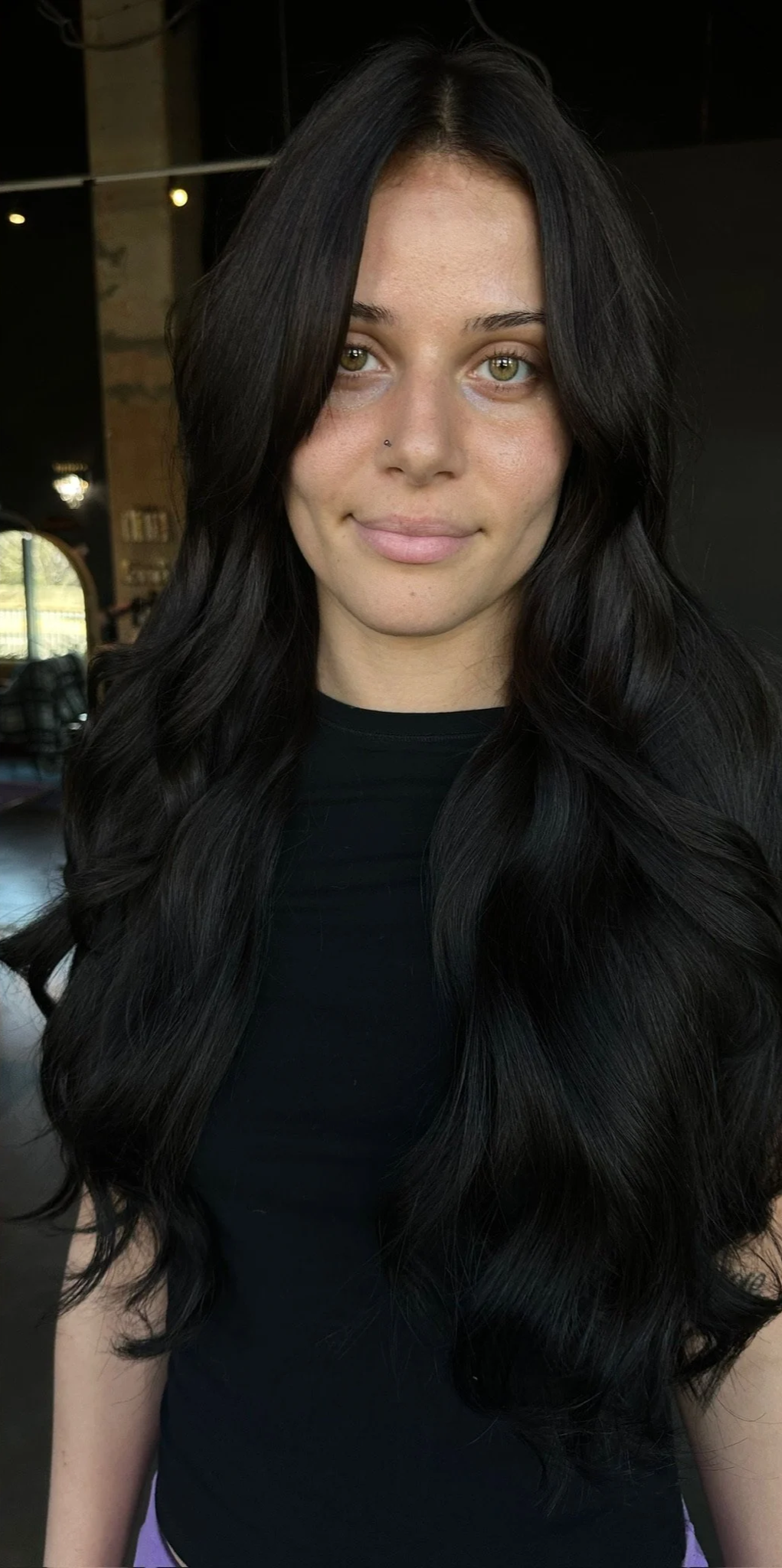 Side-by-side comparison of a woman before and after a hair transformation, showing her with long, wavy brown hair on the left and long, wavy black hair on the right. hair extensions Decatur Georgia salon hairstylist 