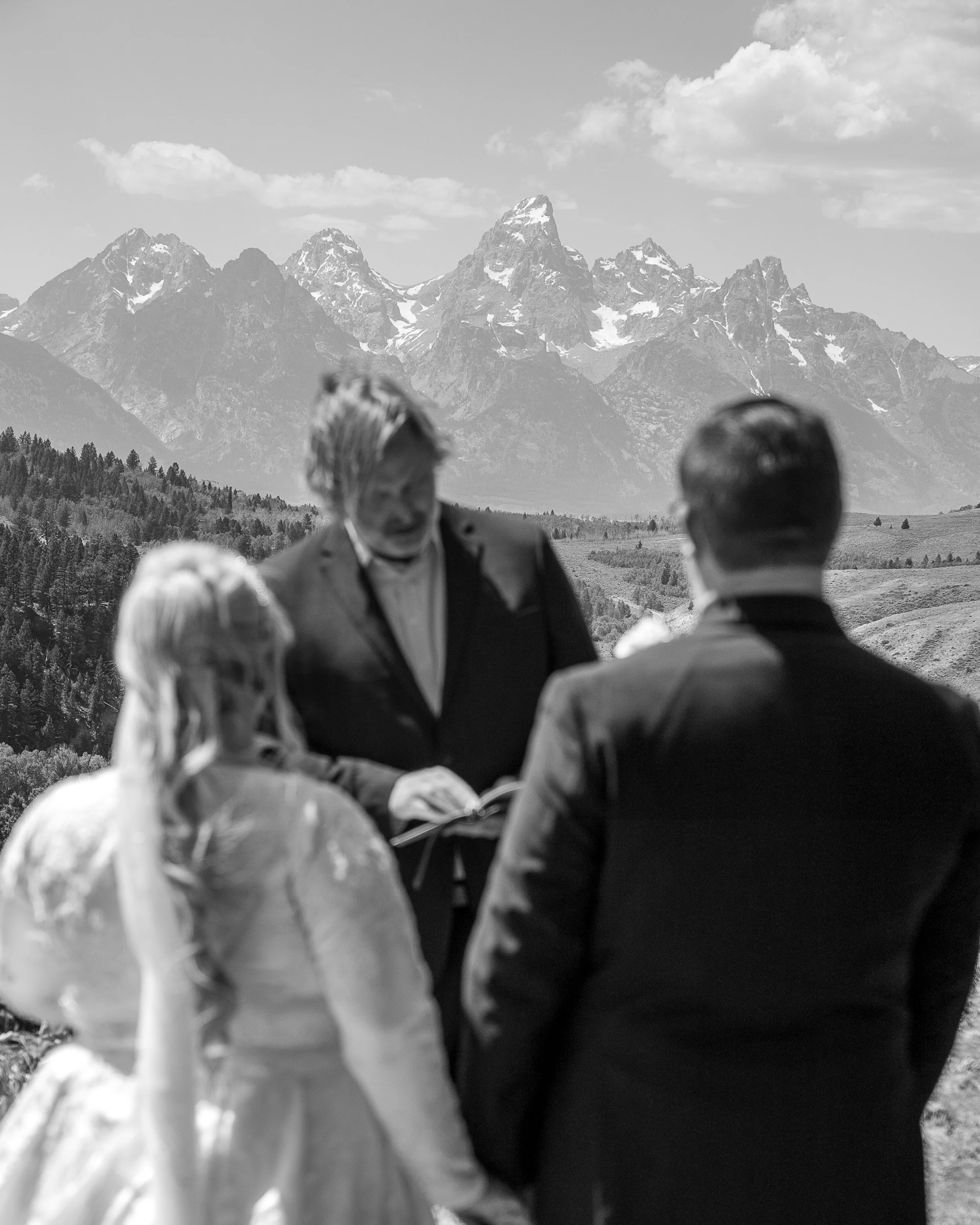 A wedding ceremony outdoors with mountains in the background, featuring a couple facing an officiant.