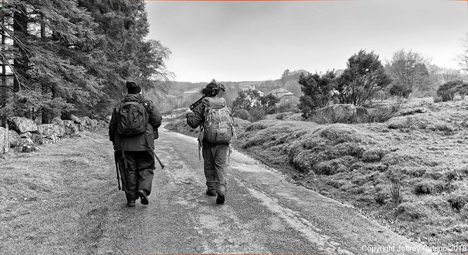 Two Photographers with backpacks walking along a rural dirt road with trees and bushes on either side. On a Dartmoor Photography Workshop with Brian Northmore Photography