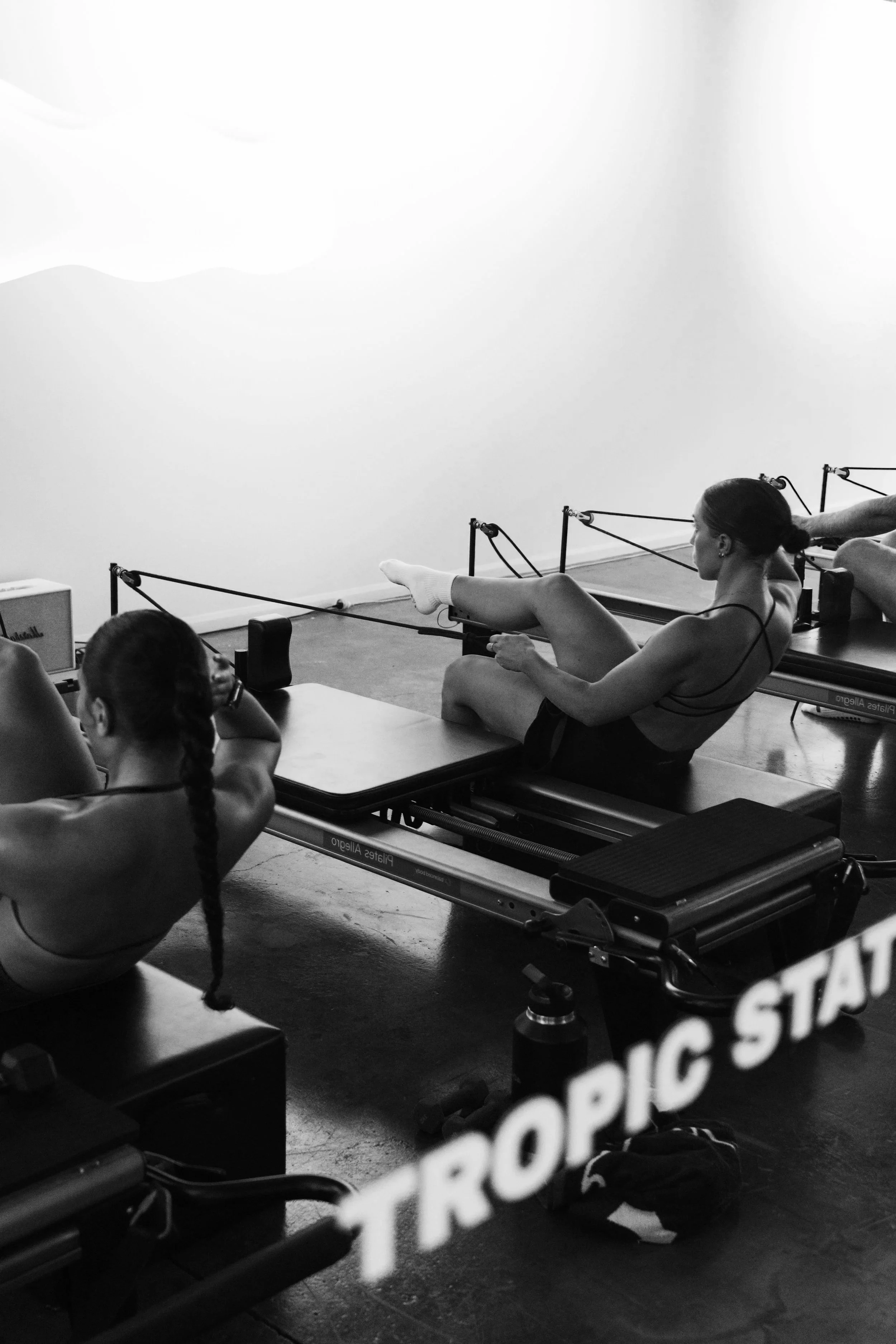 Women in workout attire doing Pilates on reformer machines in a fitness studio.