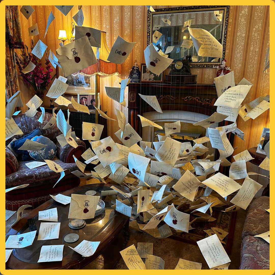 Living room with numerous floating letters and envelopes, a fireplace, mirror, framed photographs, and decorative furniture.