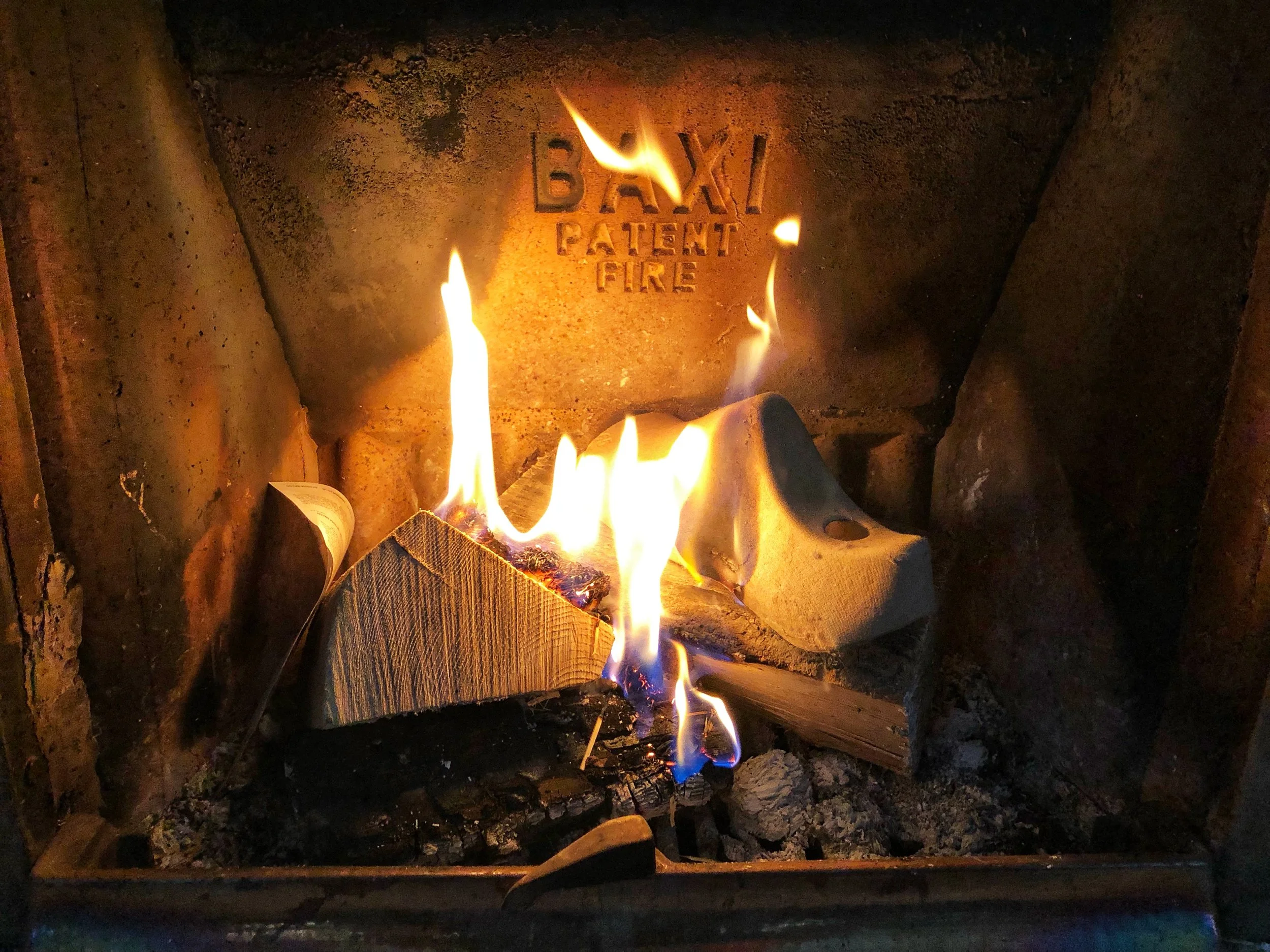 A fire burning inside a brick fireplace with the words 'BOXI PATENT FIRE' engraved on the brick behind the flames.