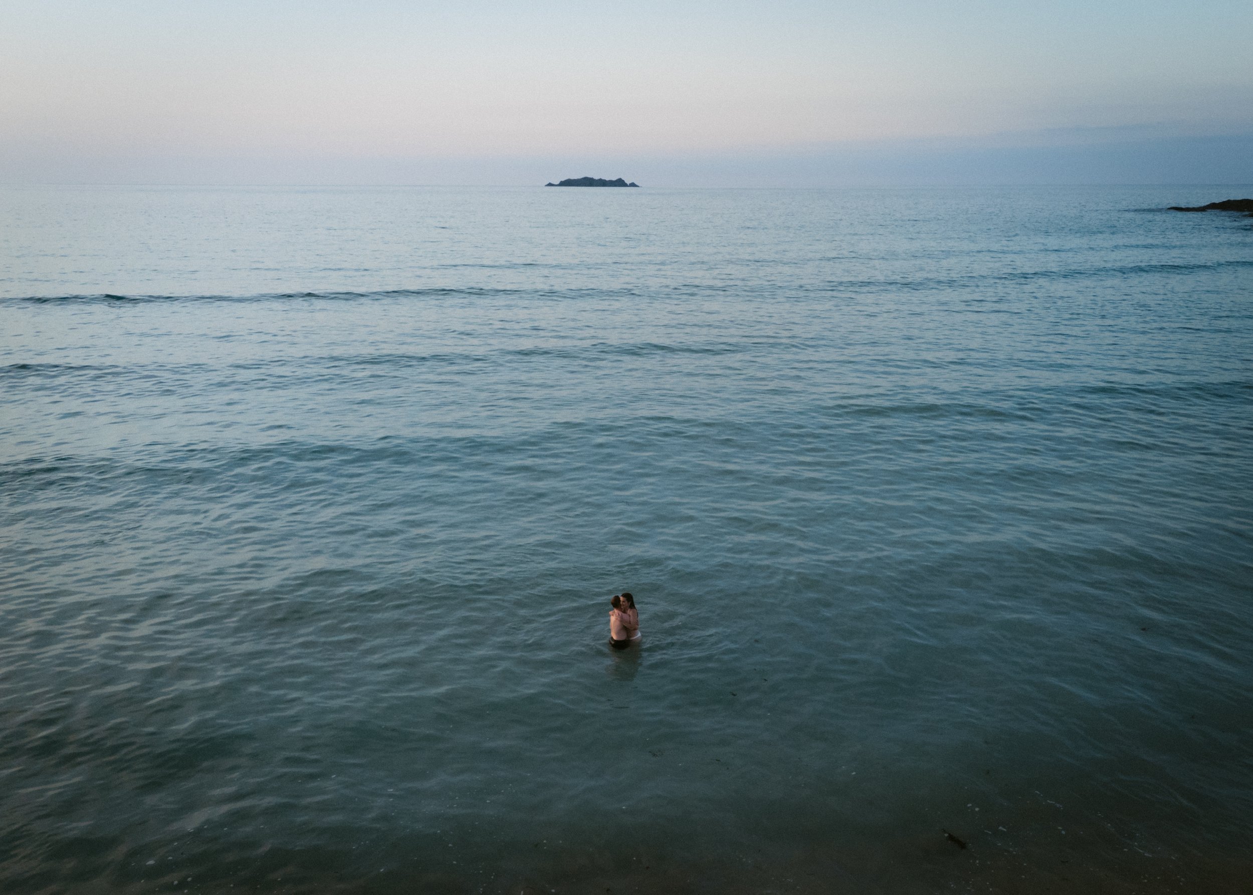 dreamy drone shots of a couple swimming in the sea together after their wedding at sunset in cornwall