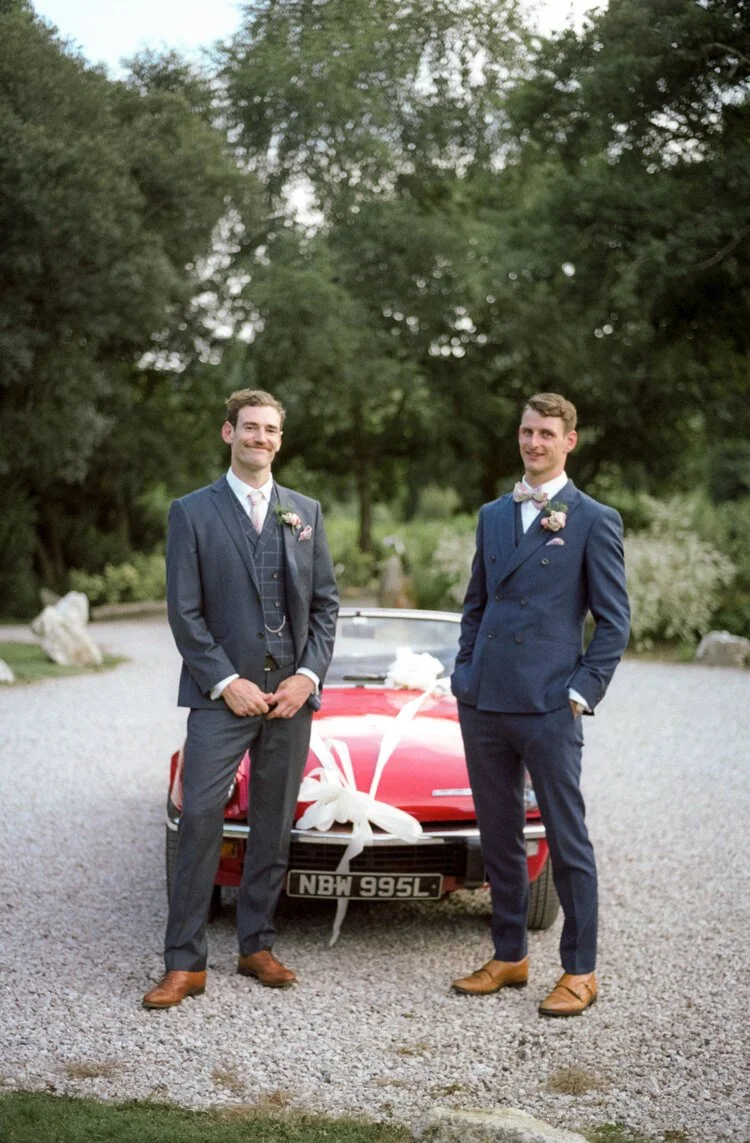 wedding captured on film at Chycara in cornwall with best man and groom standing in front of a retro sports car
