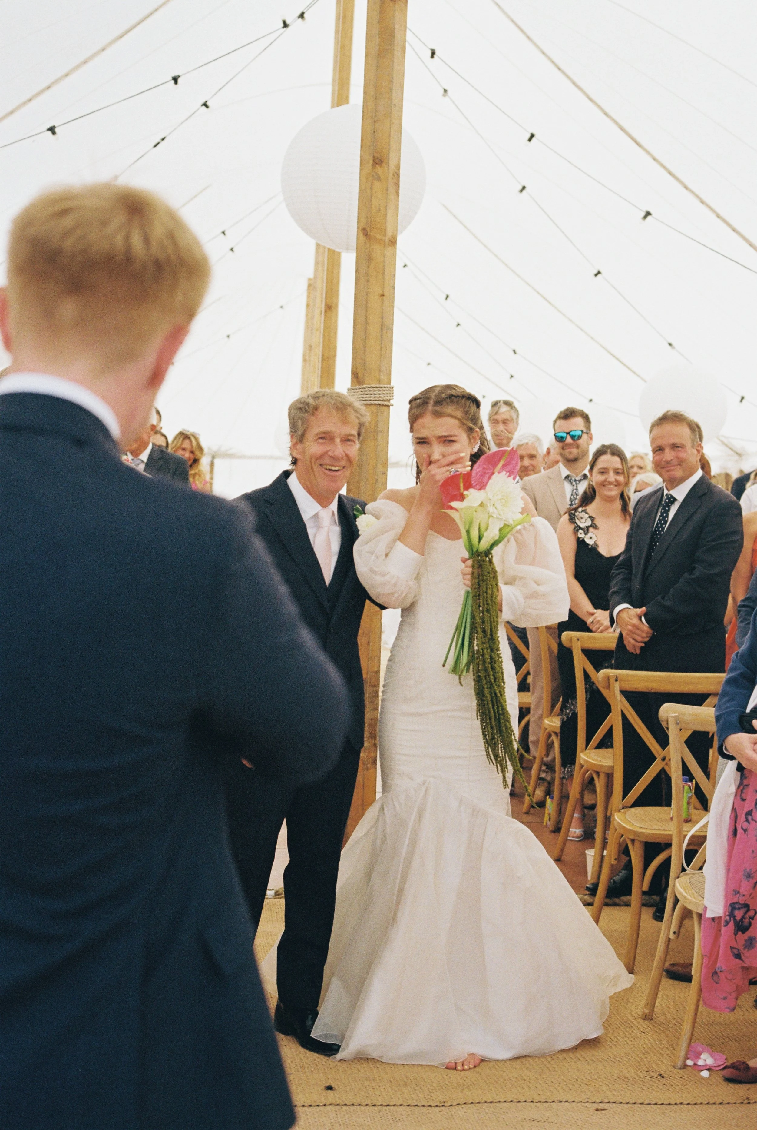 first look at the end of the aisle at a summer marquee beach wedding