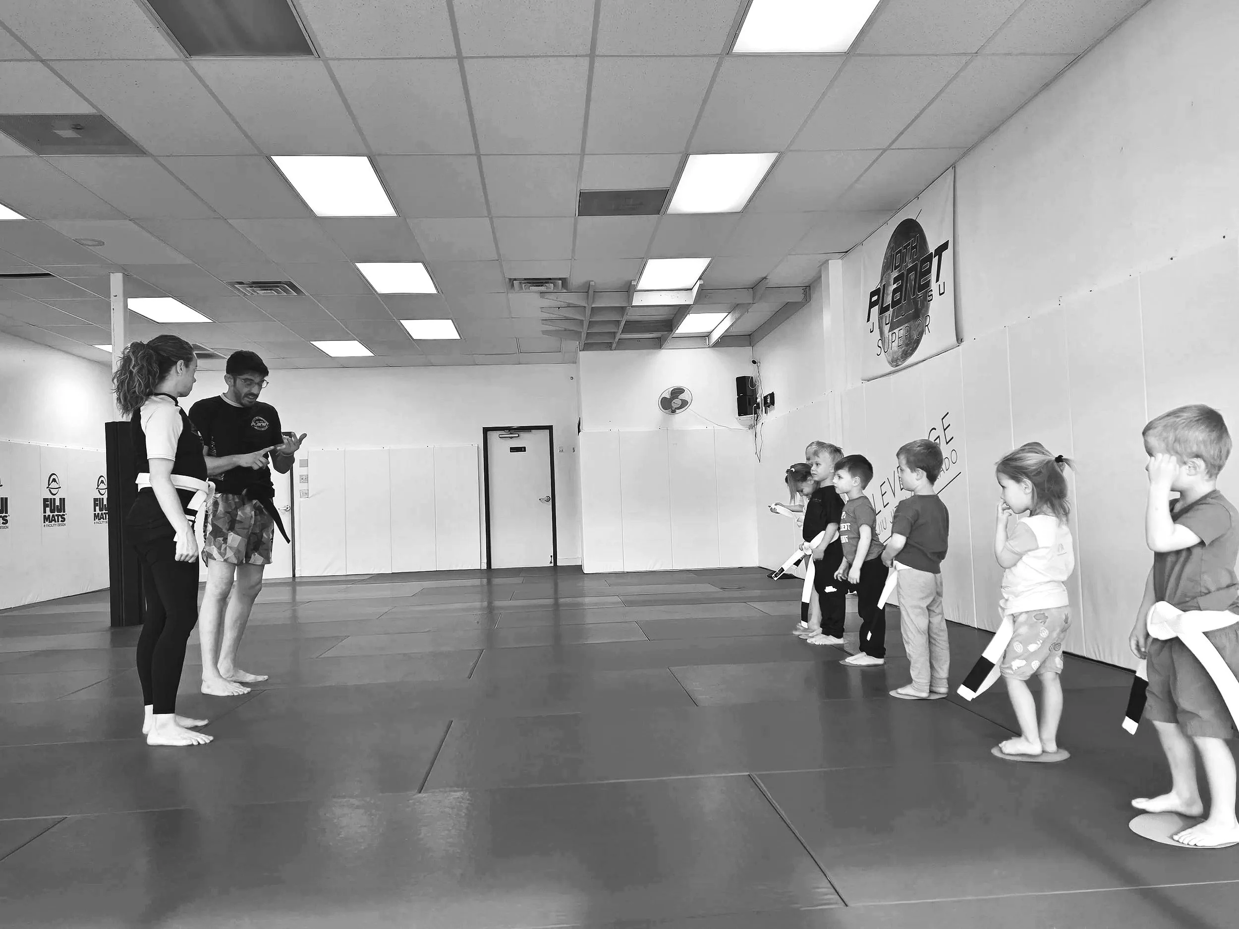 Group of six children and two adults standing in a martial arts gym
