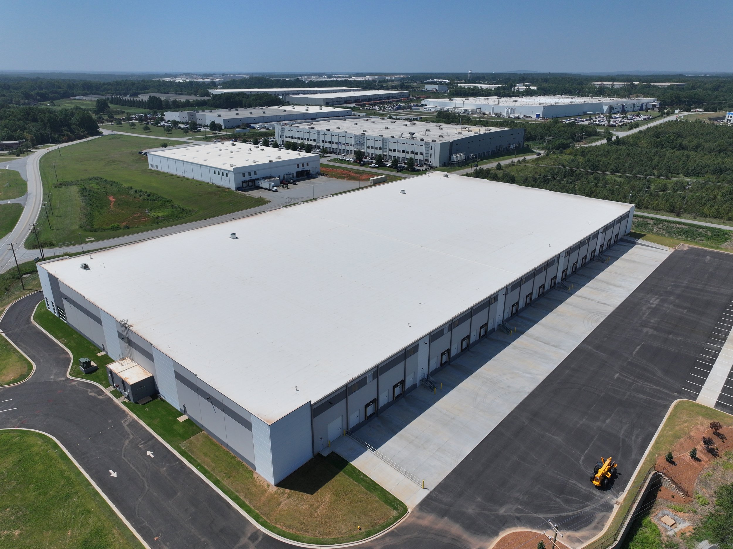 Aerial view of a large warehouse with loading docks and surrounding industrial buildings, parking lots, and green spaces.