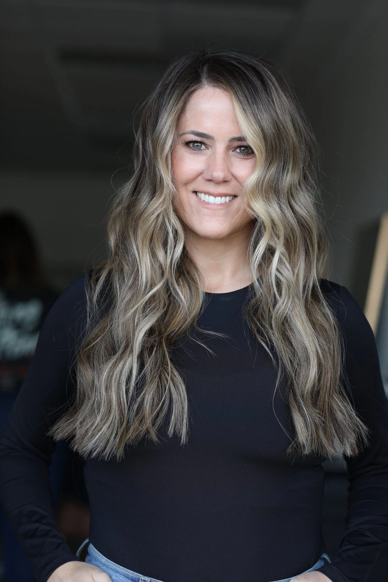 A woman with long, wavy blonde hair wearing a black top and smiling at the camera.