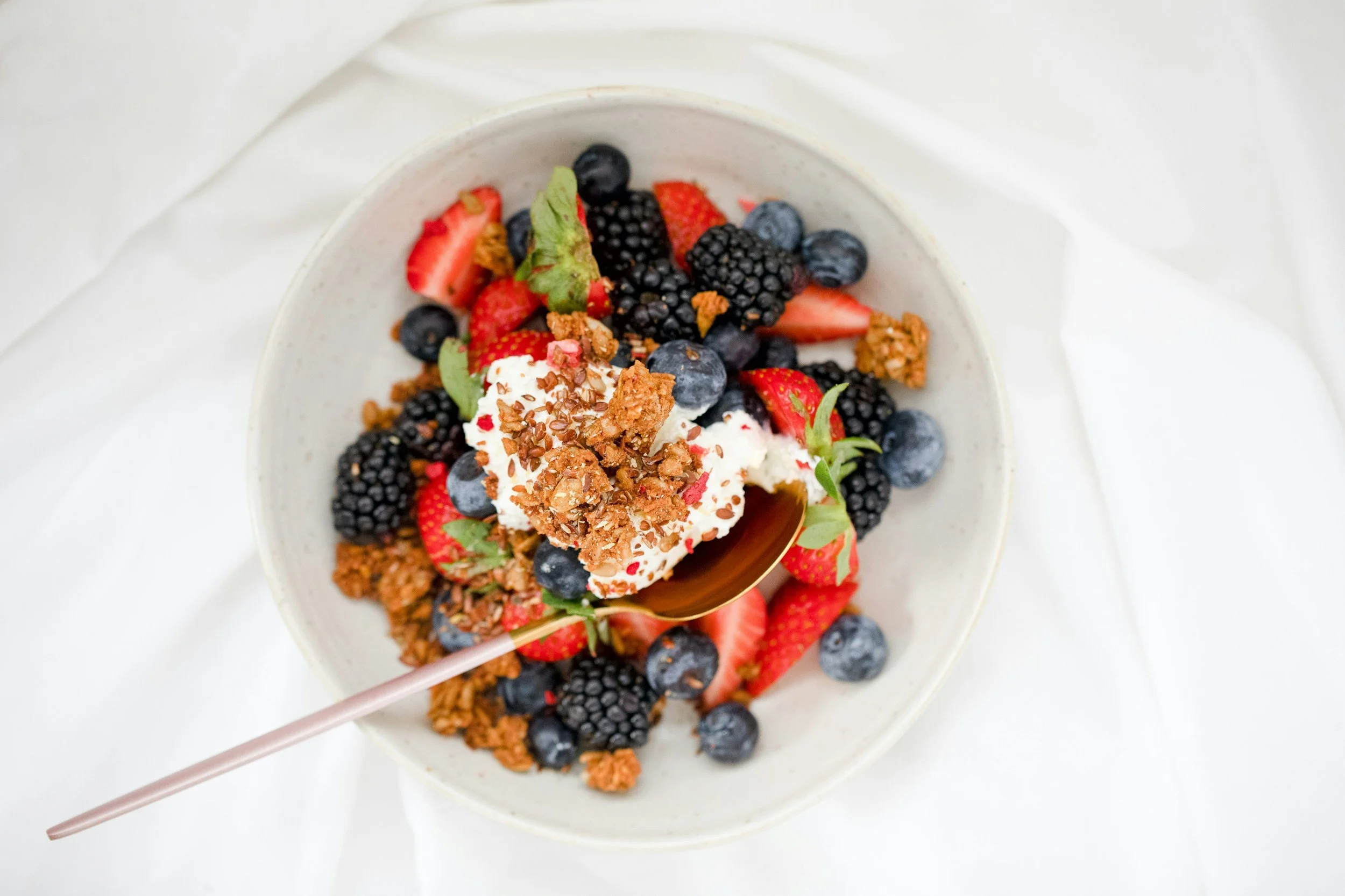 A spoon in a bowl of berries with a dollop of yoghurt sprinkled with seeds.