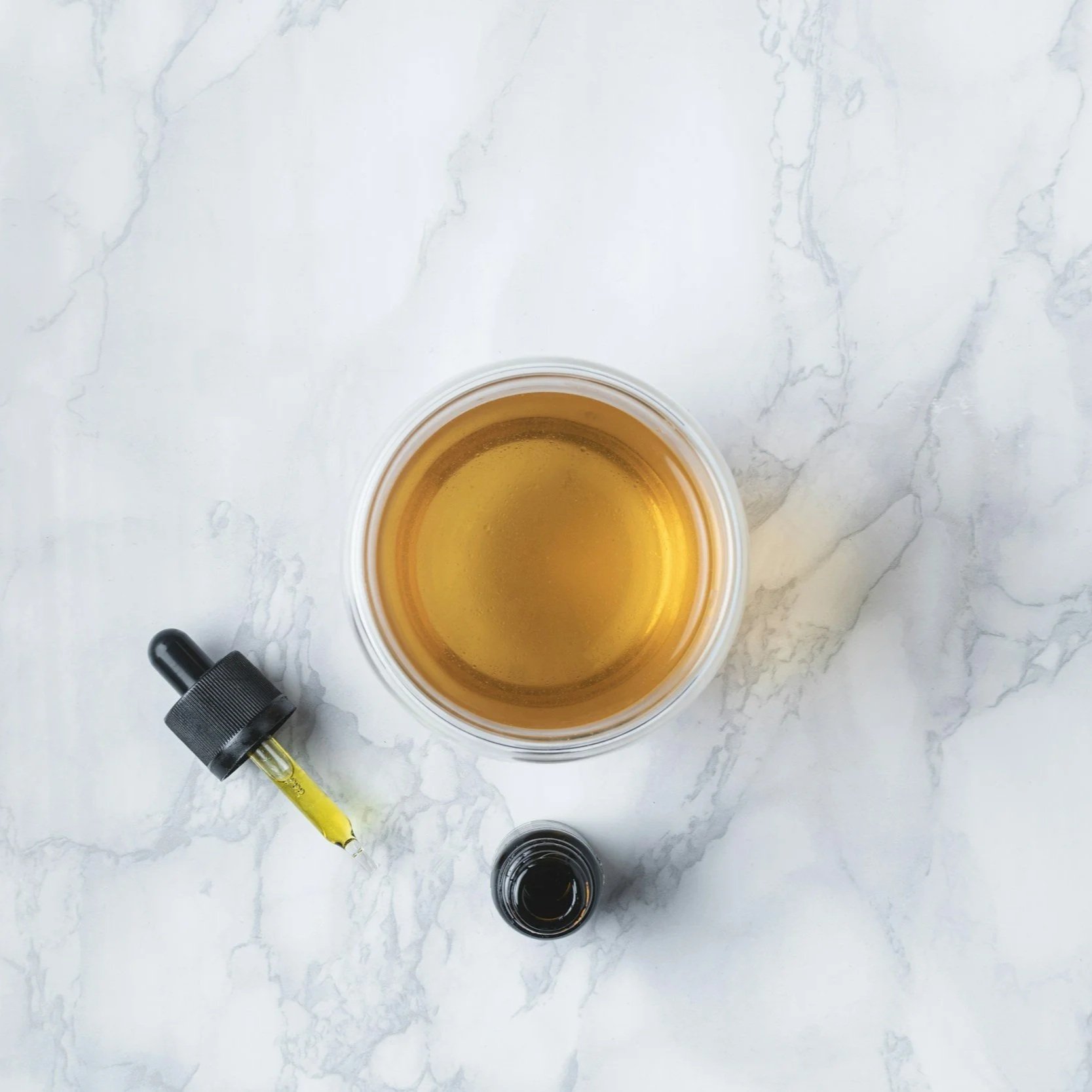 View from above of glass of CBD oil alongside small bottle and pipette.