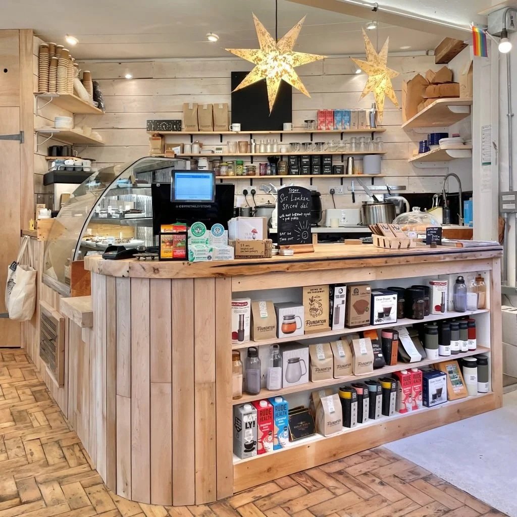 Interior of a small health food café with a wooden counter and shelves stocked with packaged goods, reusable bottles and coffee products.