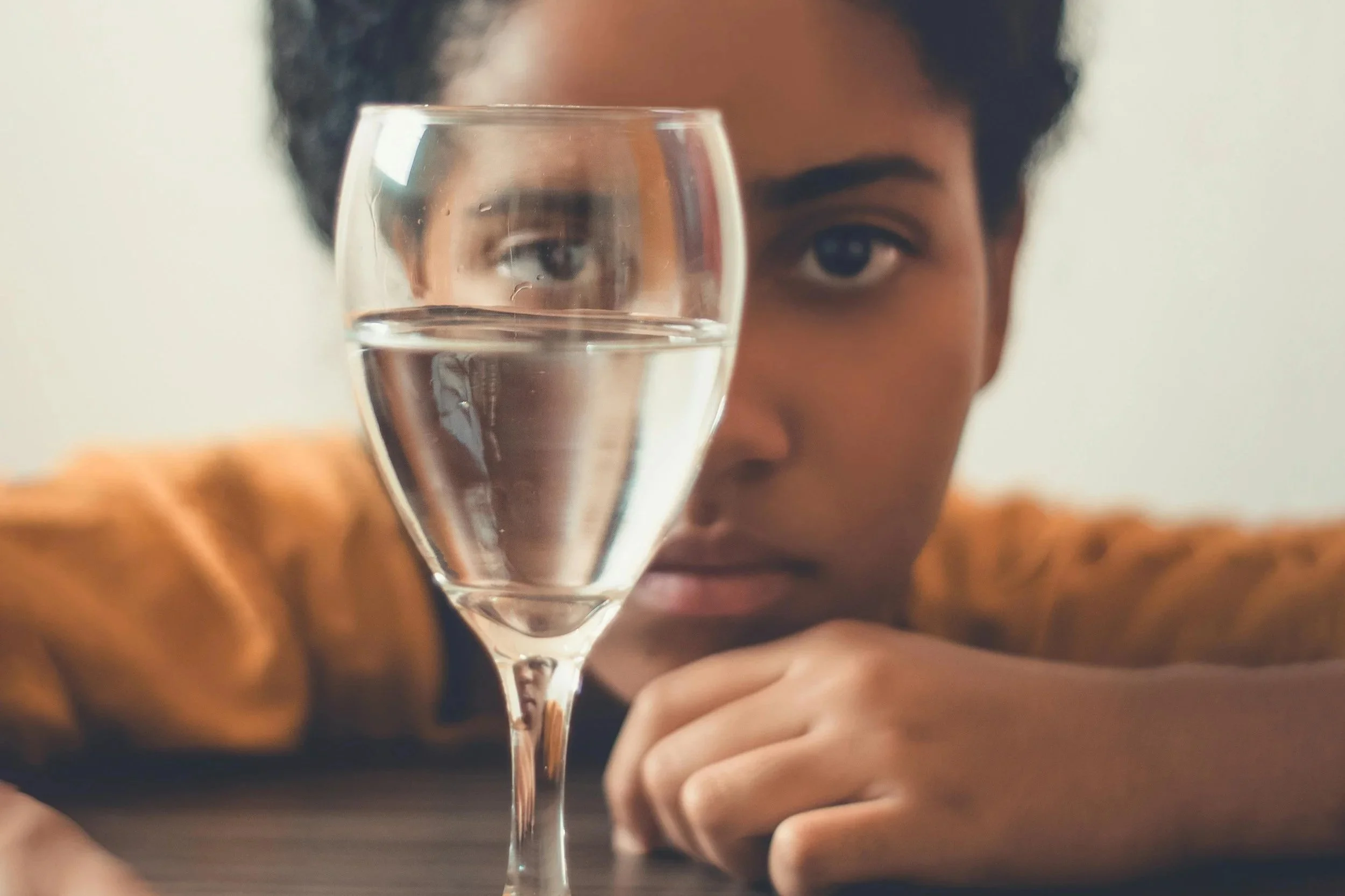 A woman gazes at a wine glass half full of water.