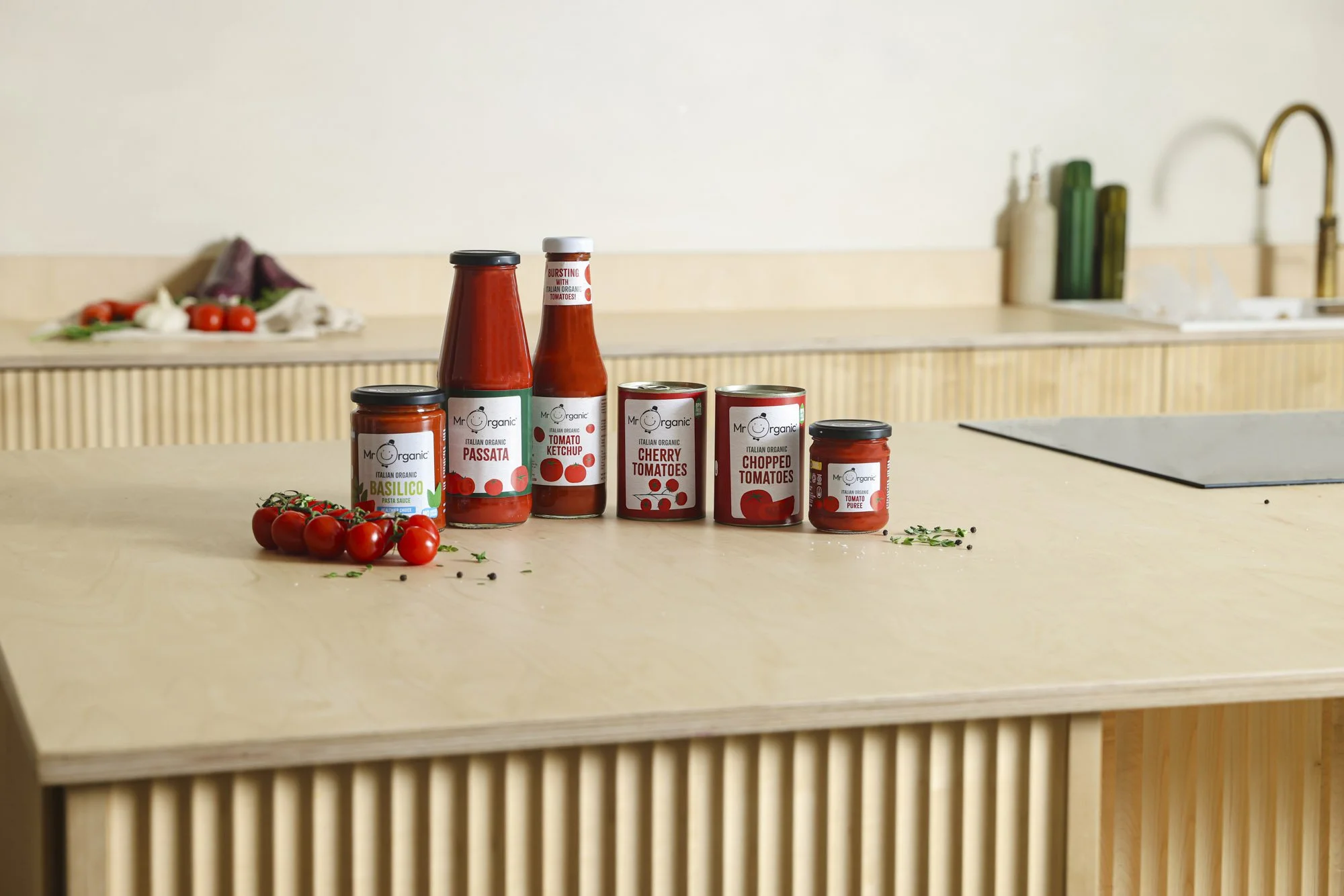 Mr Organic tomato sauces and canned tomatoes displayed on a kitchen counter with fresh vine tomatoes.